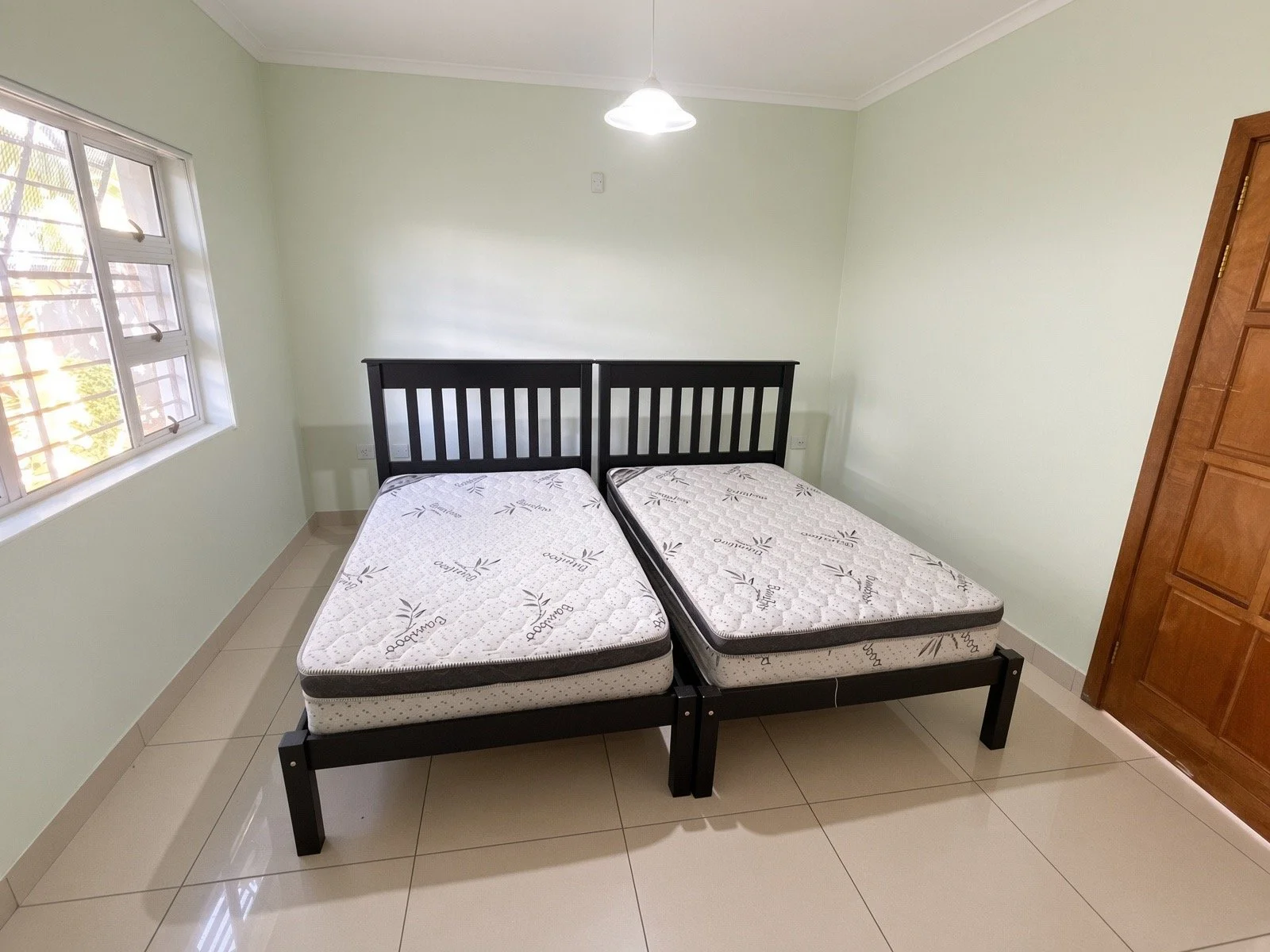 Bedroom with two single beds, window and mint walls in the 4-bedroom house for rent in a gated estate, Phakalane. Nestgeeks.