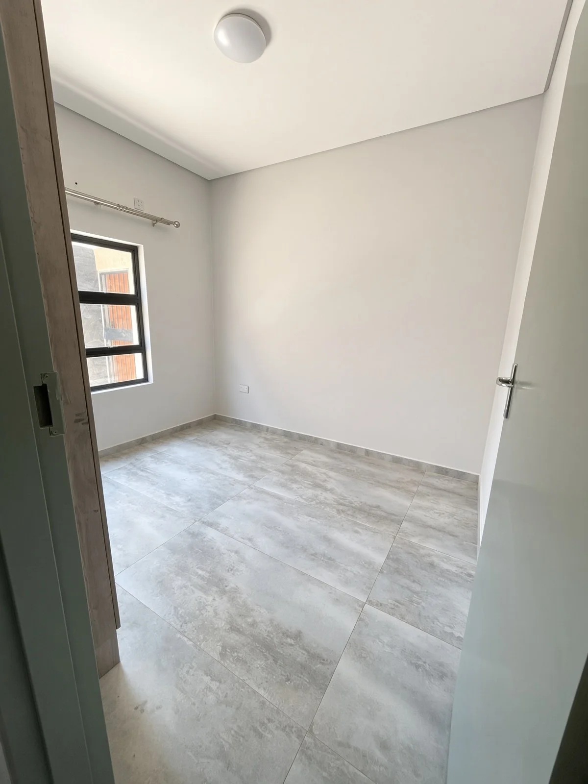 Bright bedroom with window and marble-effect floor tiles in a Maruapula house for rent