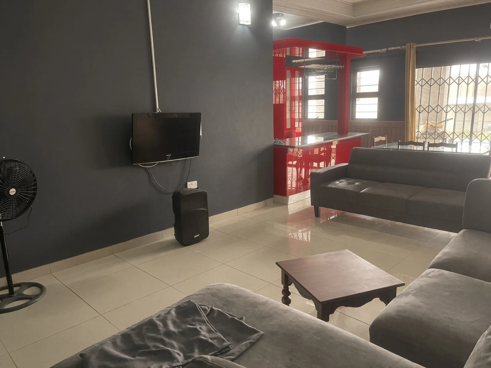 Entertainment room with grey sofas, wall-mounted TV and red kitchen beyond, Gaborone North home