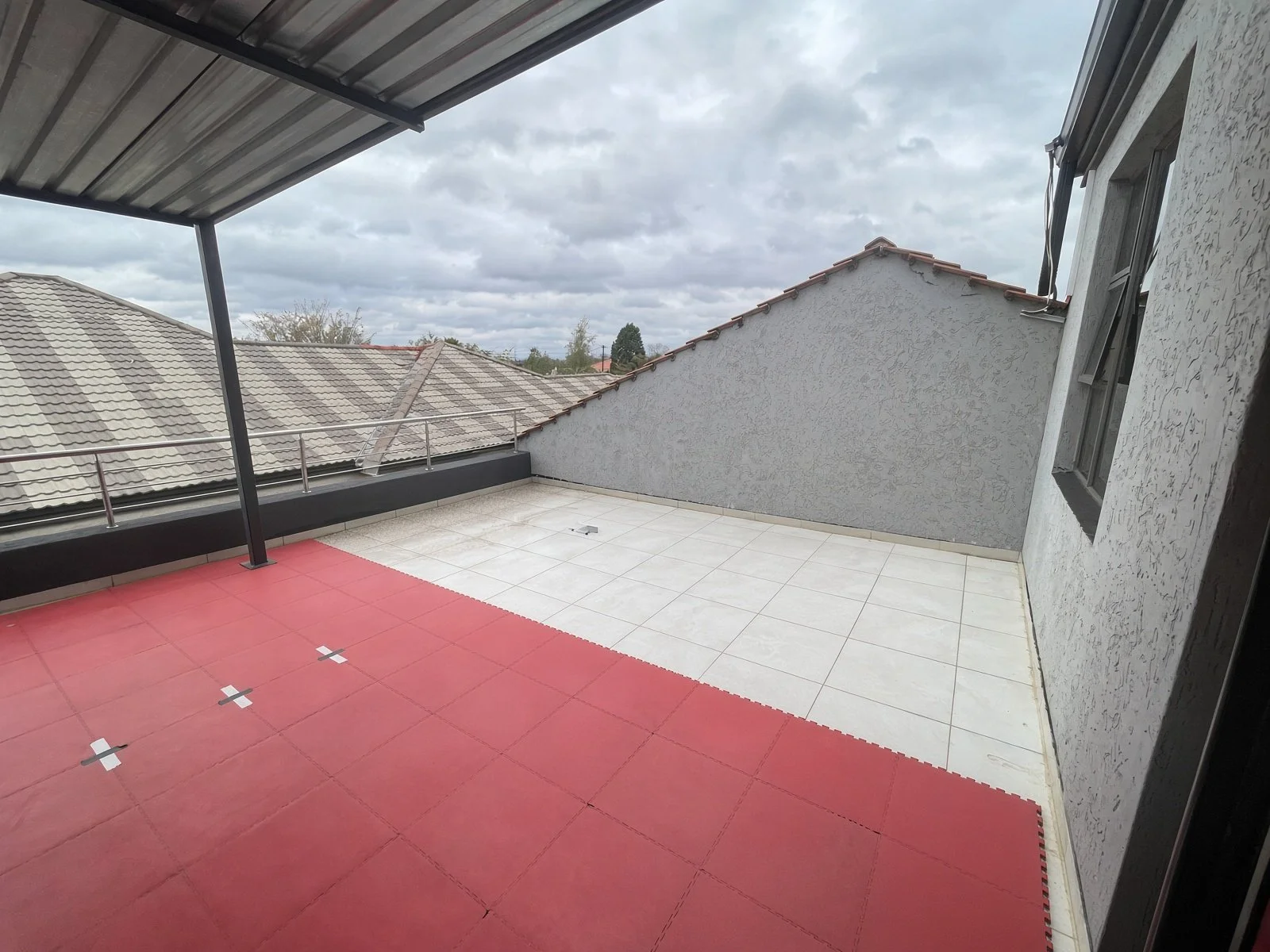 Private rooftop terrace with red interlocking mats, white tiles and neighbour views, Gaborone house for sale