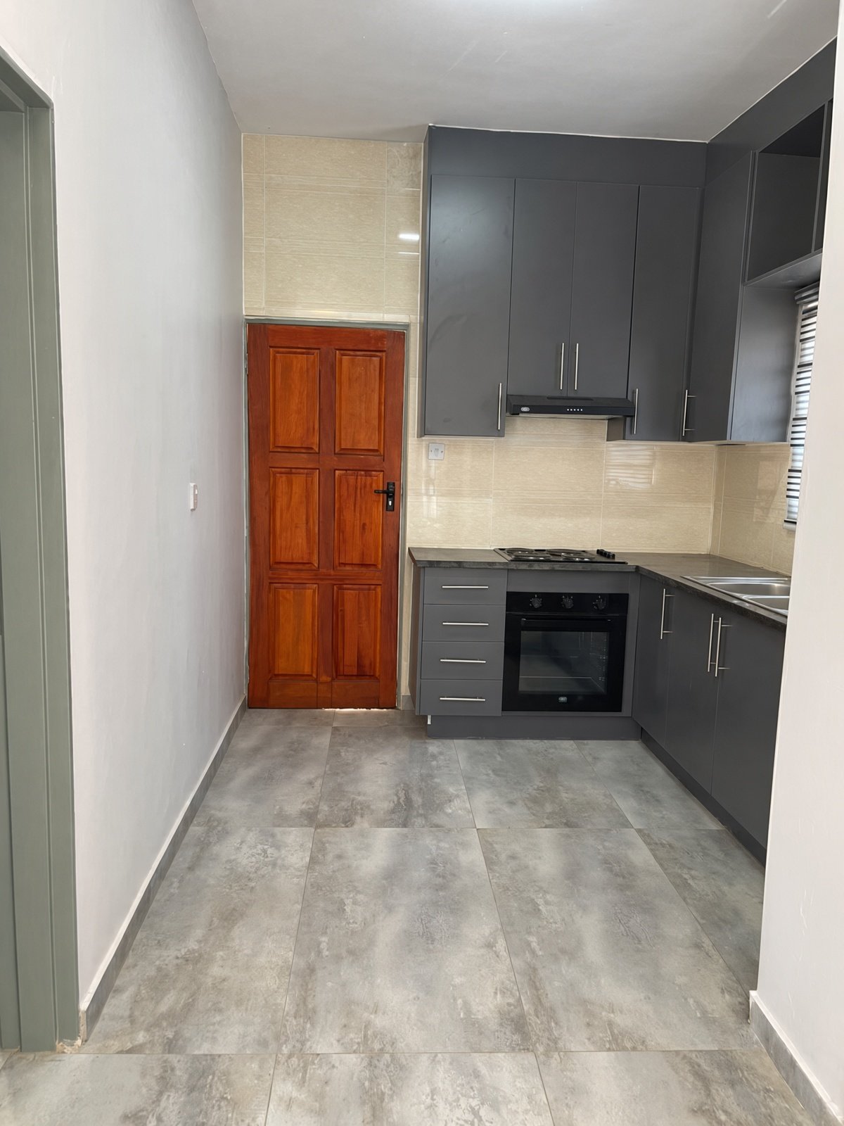 Modern grey kitchen with black counters, oven and wooden door in a house for rent in Maruapula