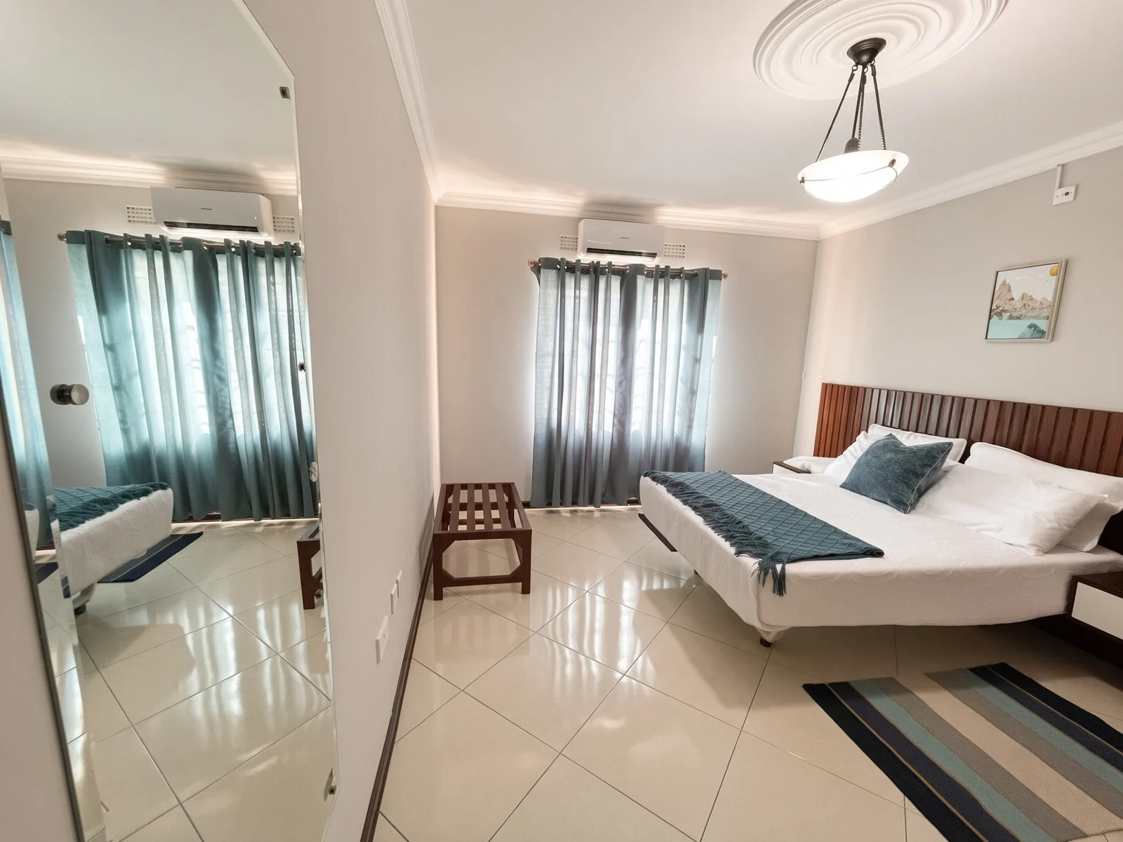 Air-conditioned bedroom with wooden slat headboard, teal curtains and full-length mirror in the fully furnished 5-bedroom house for rent, Phakalane. Nestgeeks.