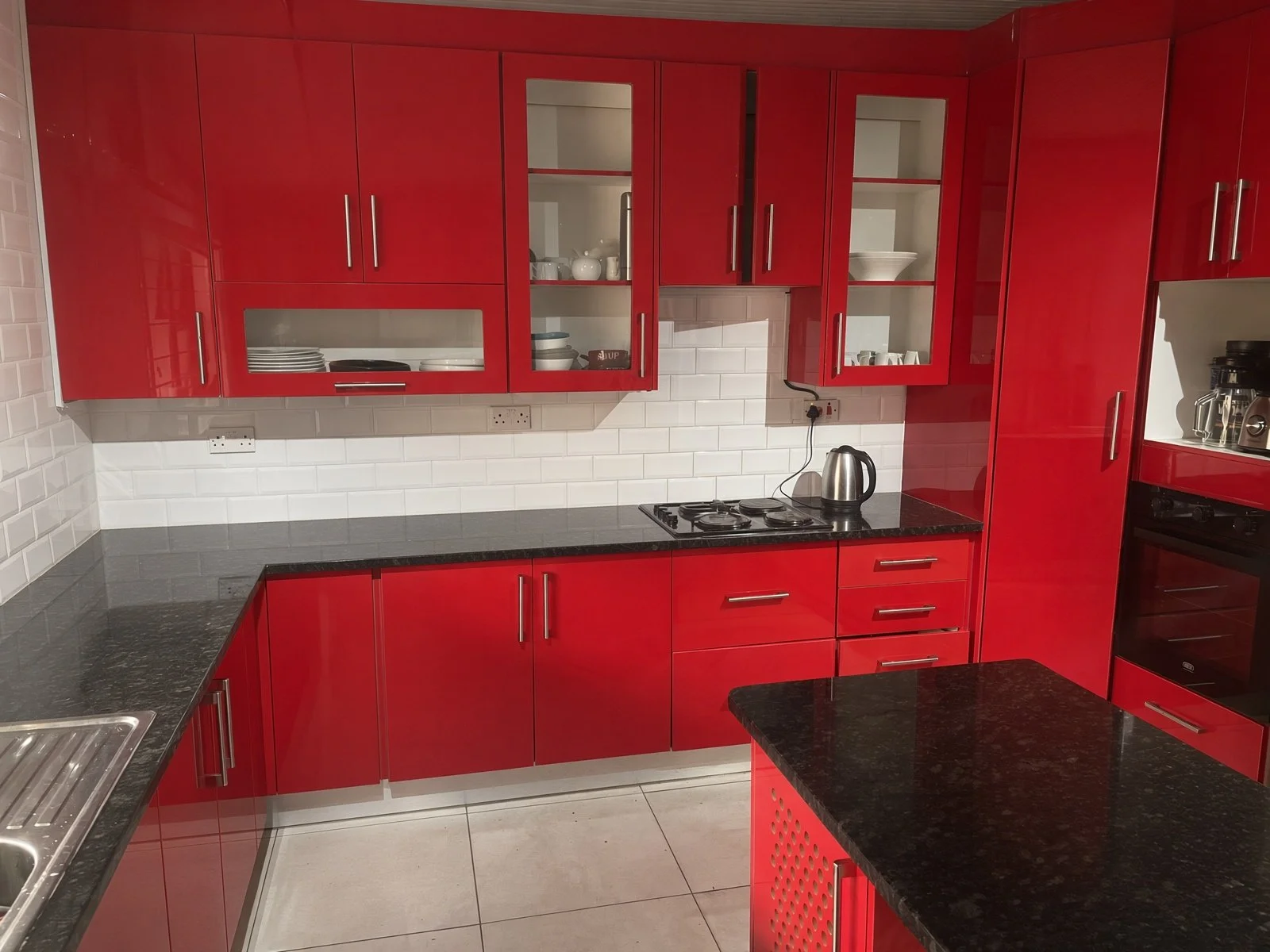 Modern high-gloss red kitchen with black granite counters, electrical stove and built-in oven, Gaborone family home