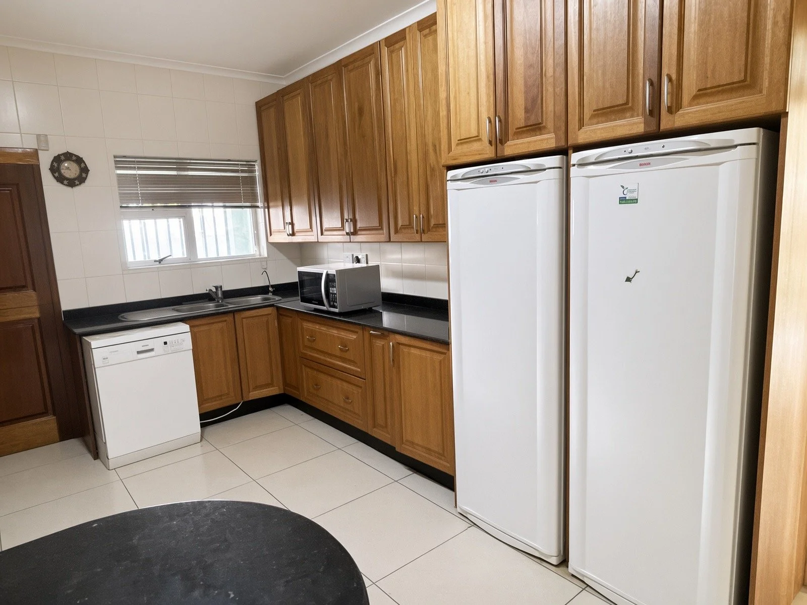 Fitted kitchen with two fridges, dishwasher, microwave and wooden units in the 4-bedroom house for rent, gated estate Phakalane. Nestgeeks.