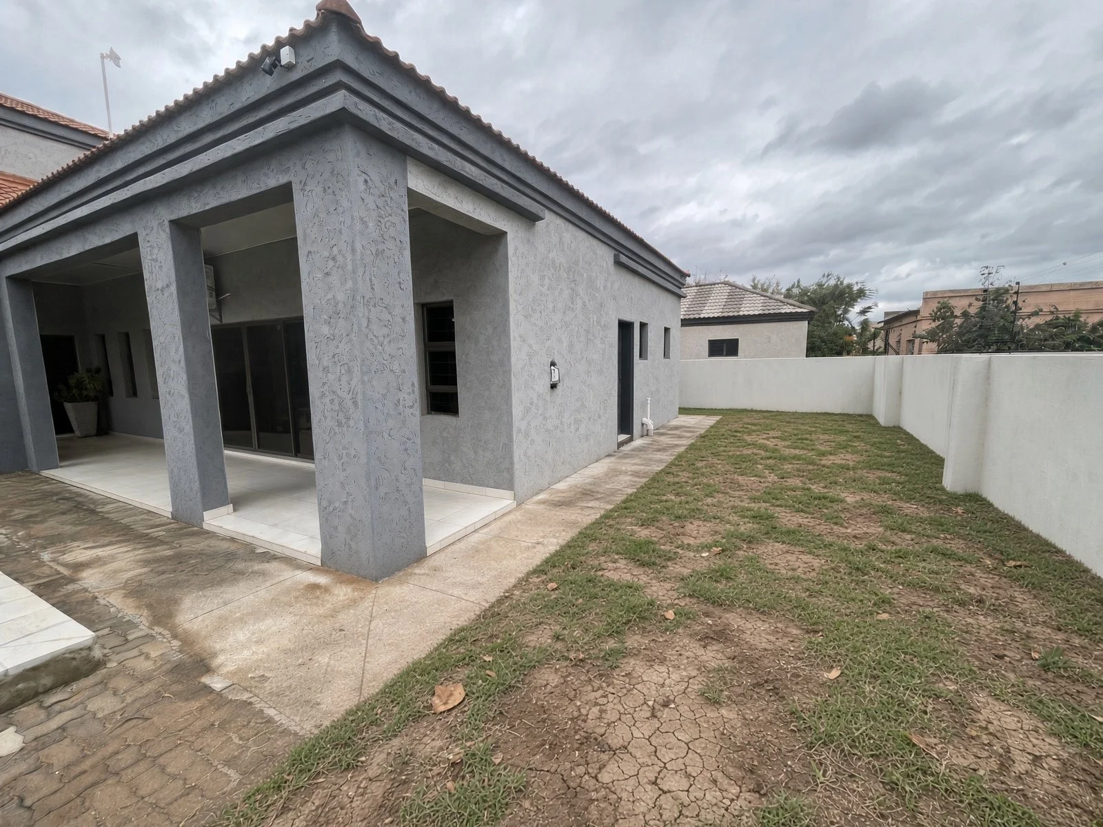 Grey rendered family house for sale in Gaborone with covered patio, tiled walkway and private walled garden