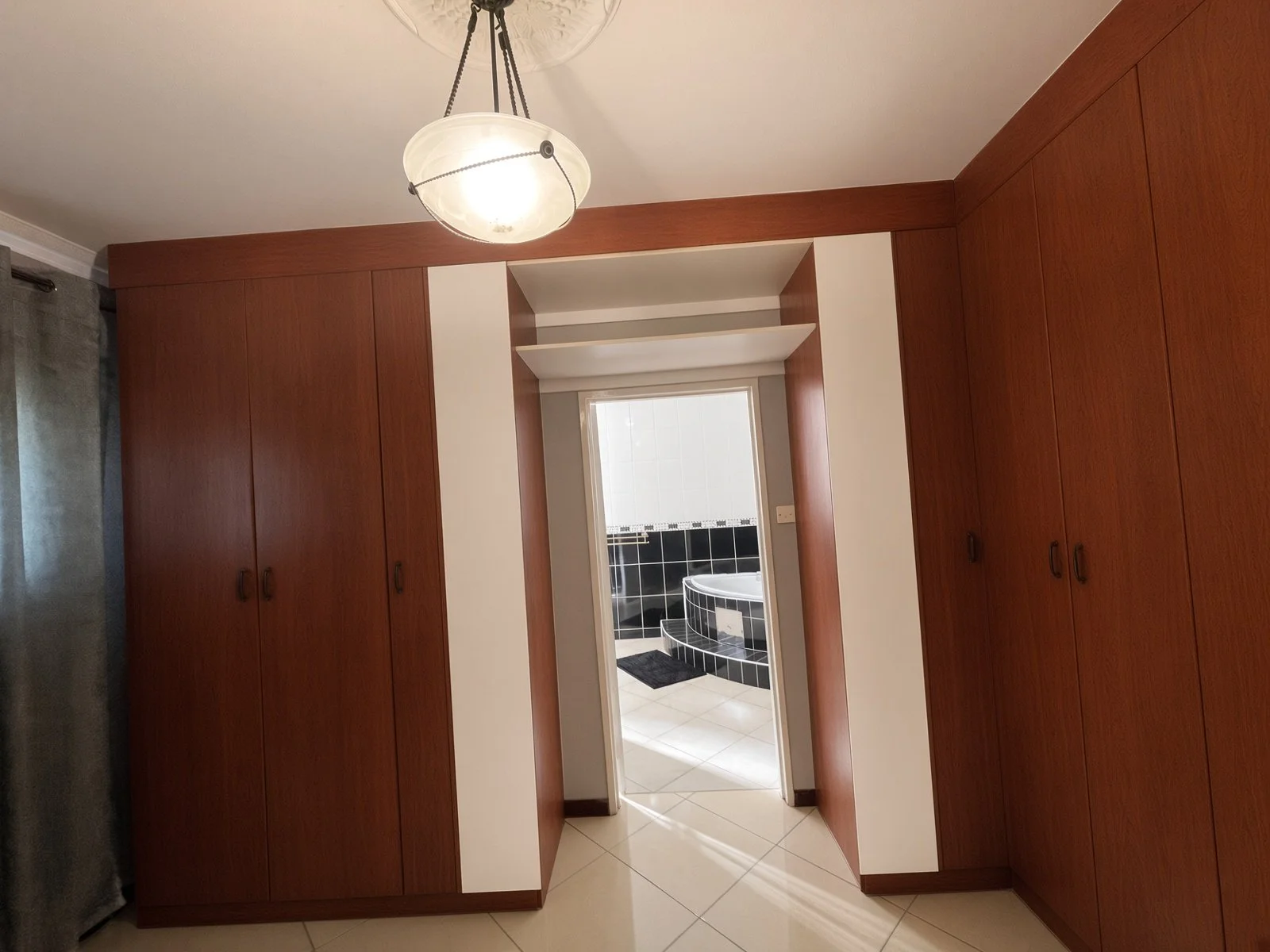 Walk-in closet with wooden fitted wardrobes leading to the master ensuite bathroom in the fully furnished 5-bedroom house for rent, Phakalane. Nestgeeks.