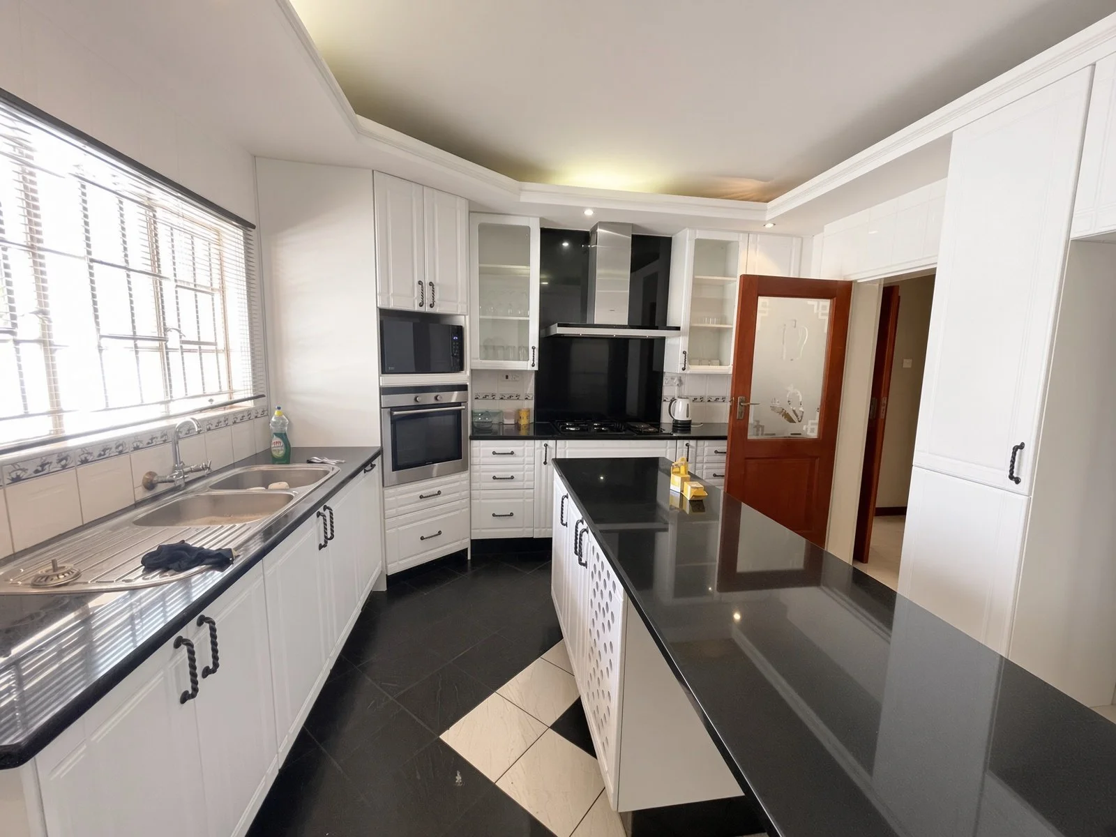 Fitted kitchen with black granite island, white cabinets, oven, hob and scullery in the fully furnished 5-bedroom house for rent in Phakalane. Nestgeeks.