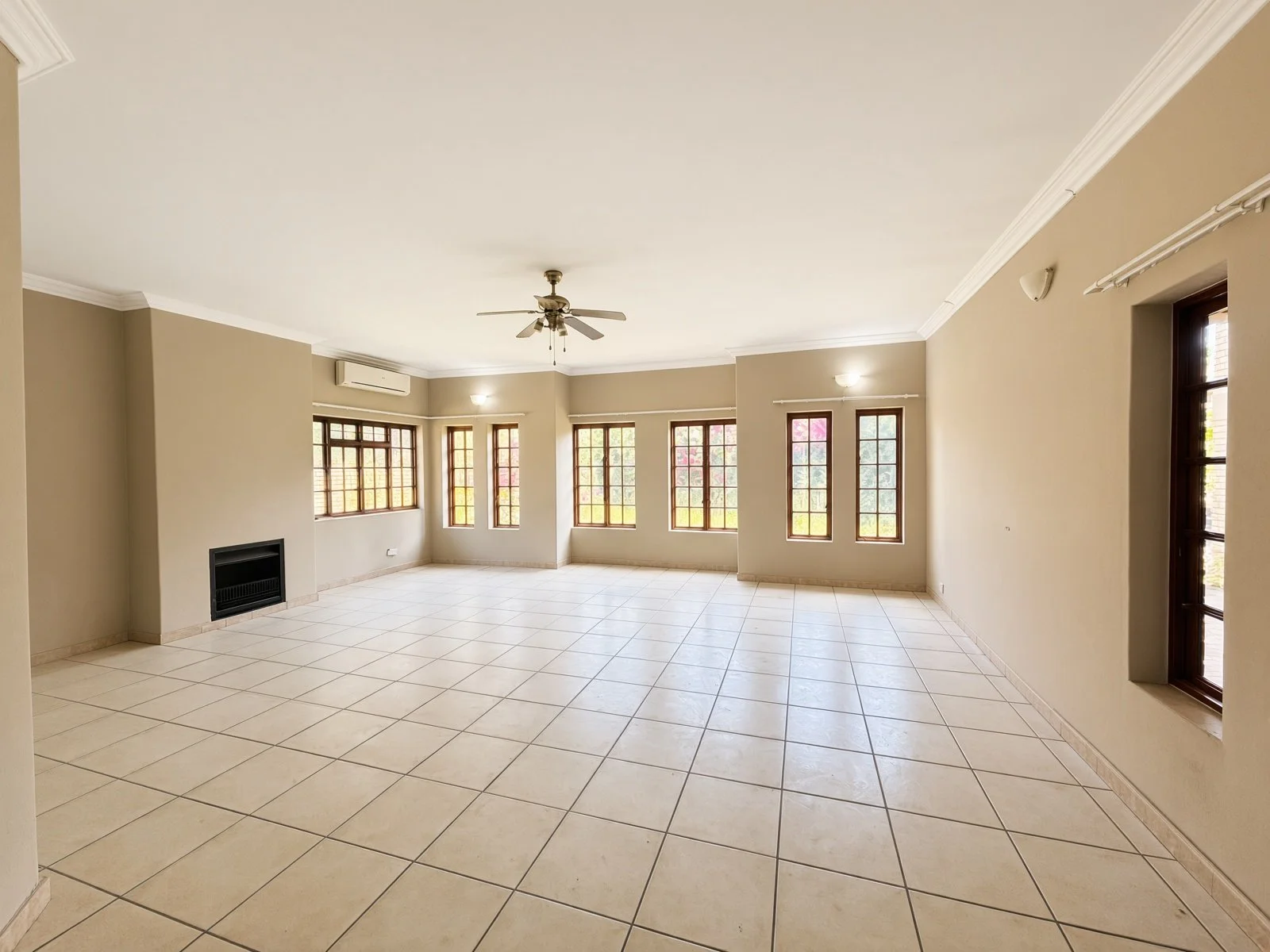 Large lounge with fireplace, ceiling fan and many windows in a Phakalane house for sale