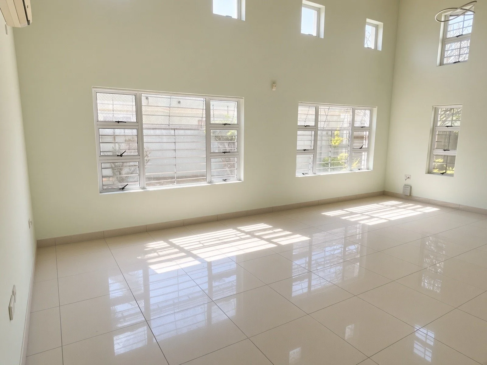 Bright double-volume living area with multiple windows and tiled floors in the 4-bedroom rental, gated estate Phakalane. Nestgeeks.