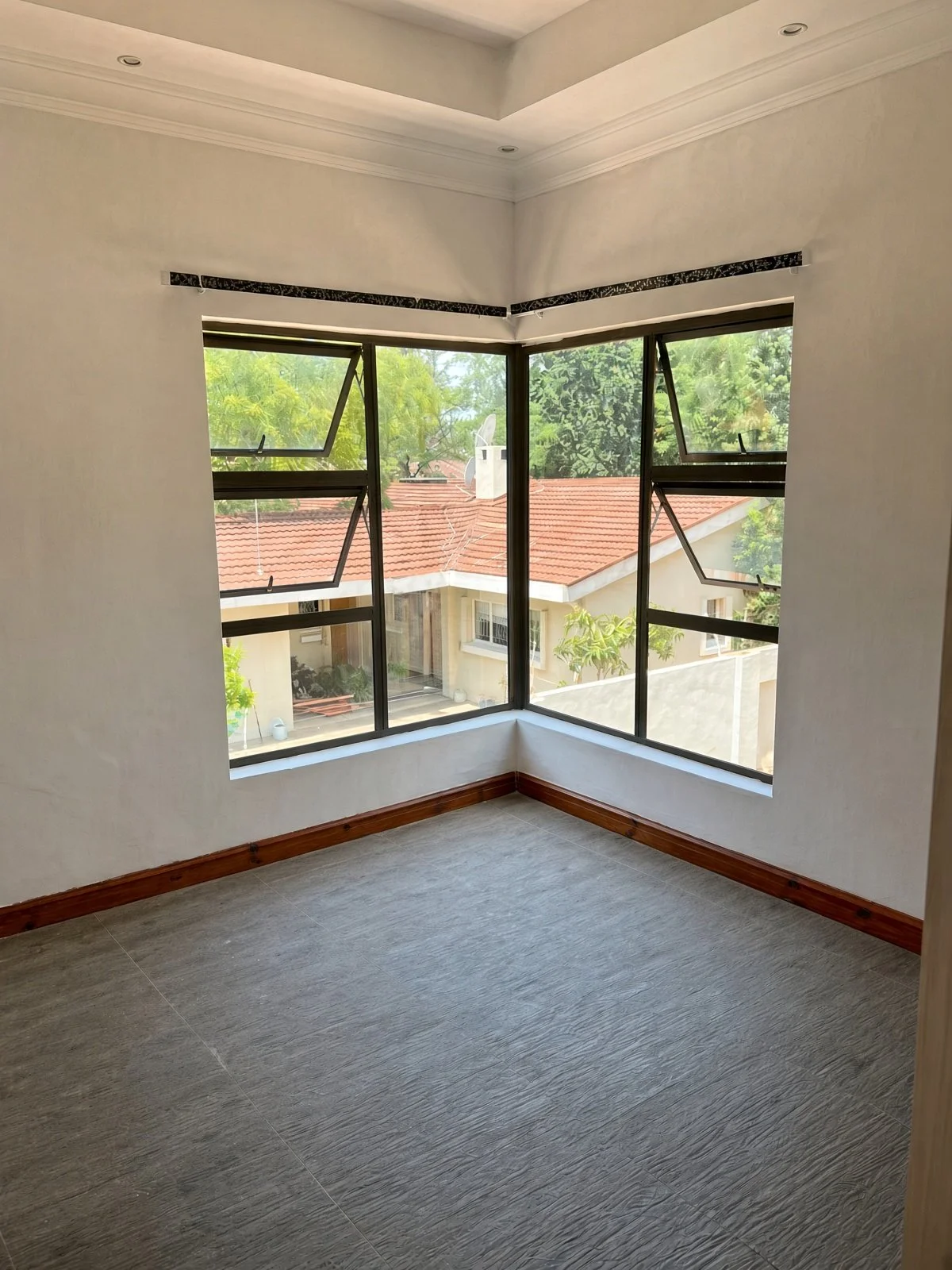 Bright corner room with large opening windows and grey wood-look tiles in a 2-bedroom apartment for rent in Extension 11 Gaborone