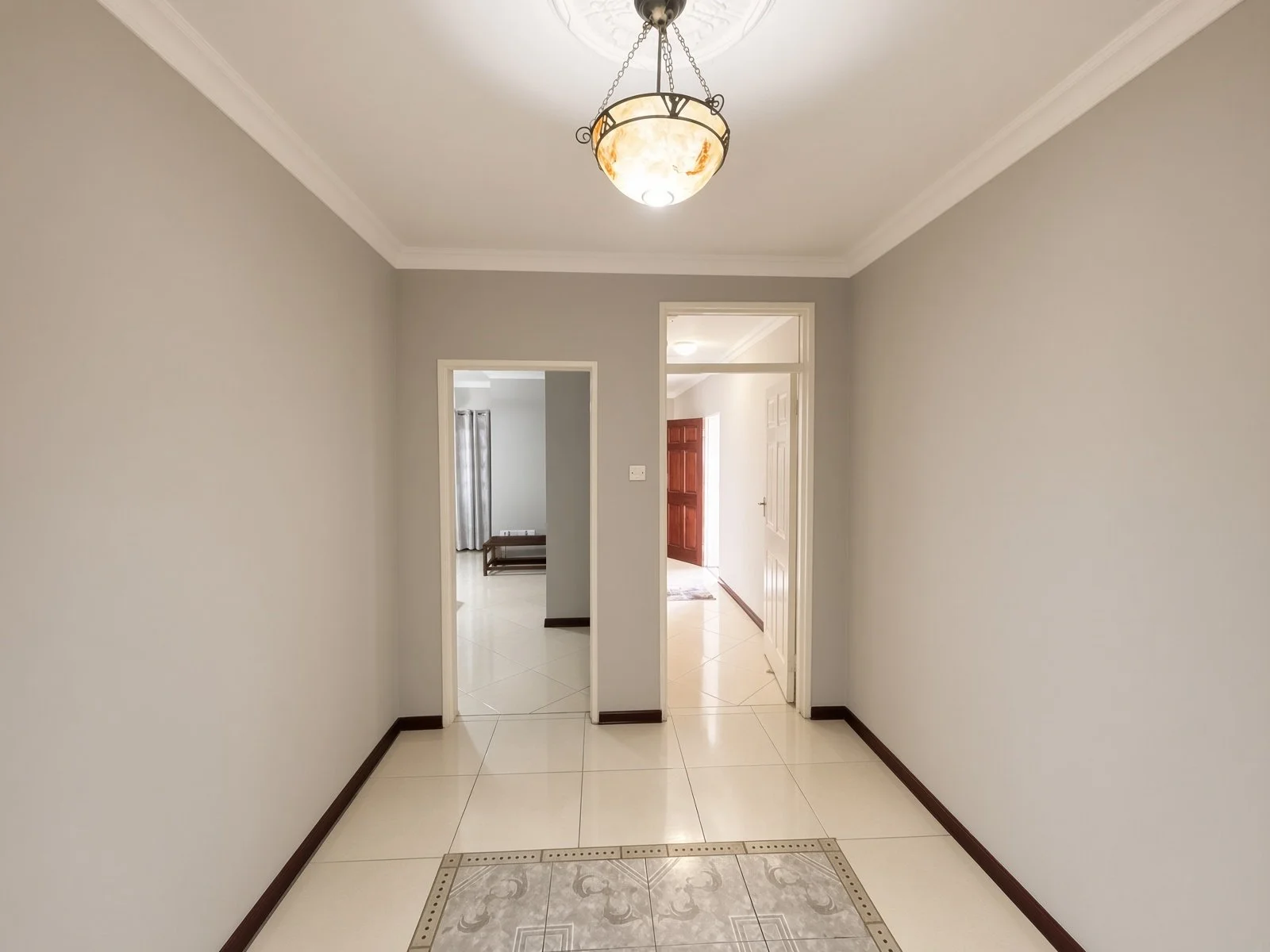 Entrance hallway with cream tiled floor, decorative inset tiles and ceiling light in a fully furnished 5-bedroom house for rent in Phakalane. Nestgeeks listing.