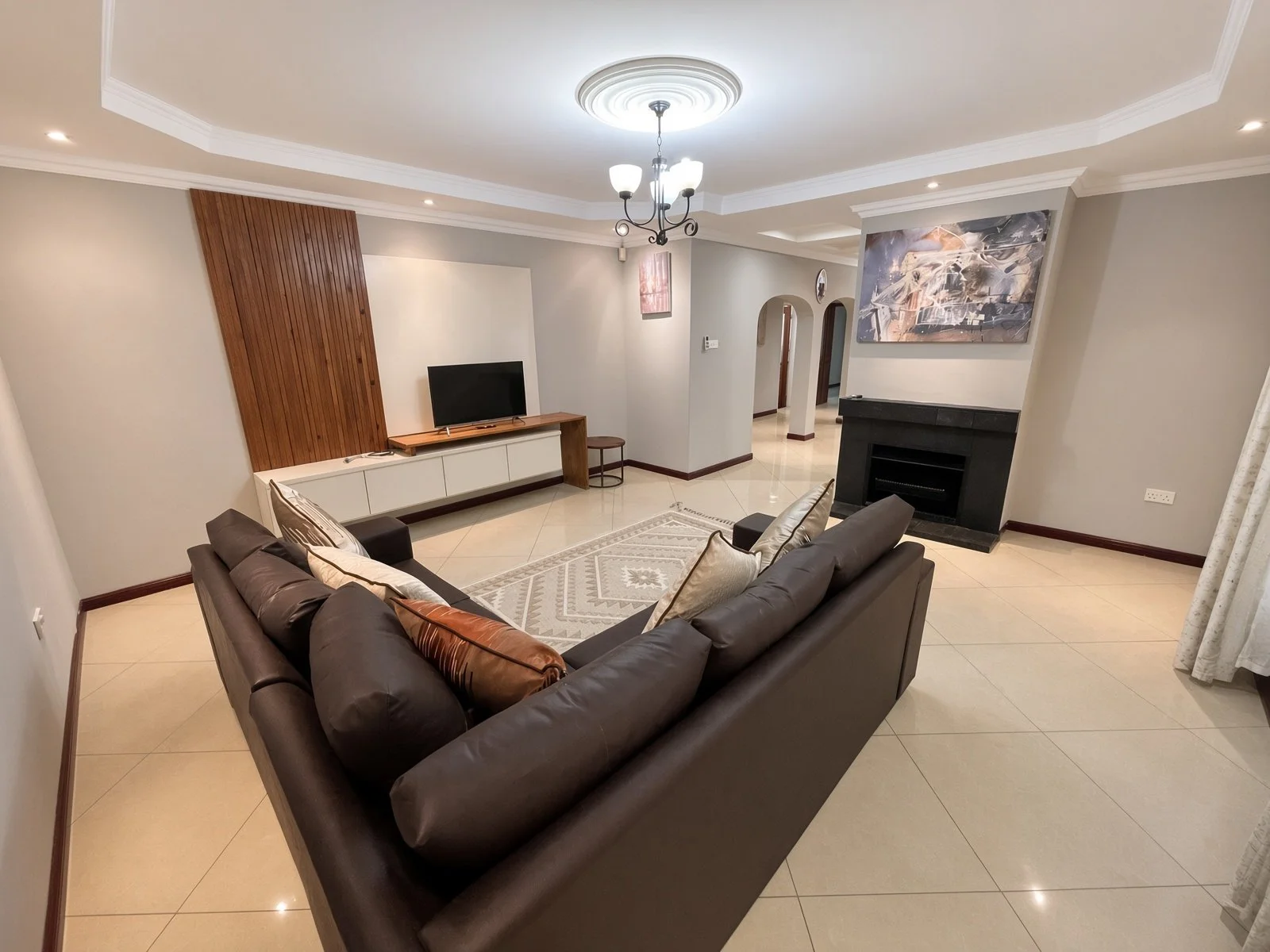 Lounge with wooden TV feature wall, fireplace and brown sofa in the fully furnished 5-bedroom Phakalane rental. Nestgeeks property.