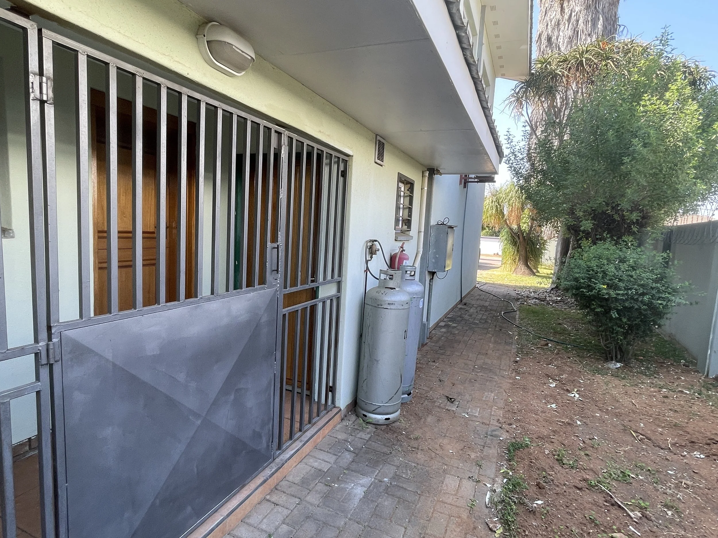 Secure side entrance with burglar gate, gas bottles and paved path at the 4-bedroom house for rent in a gated estate, Phakalane. Nestgeeks.