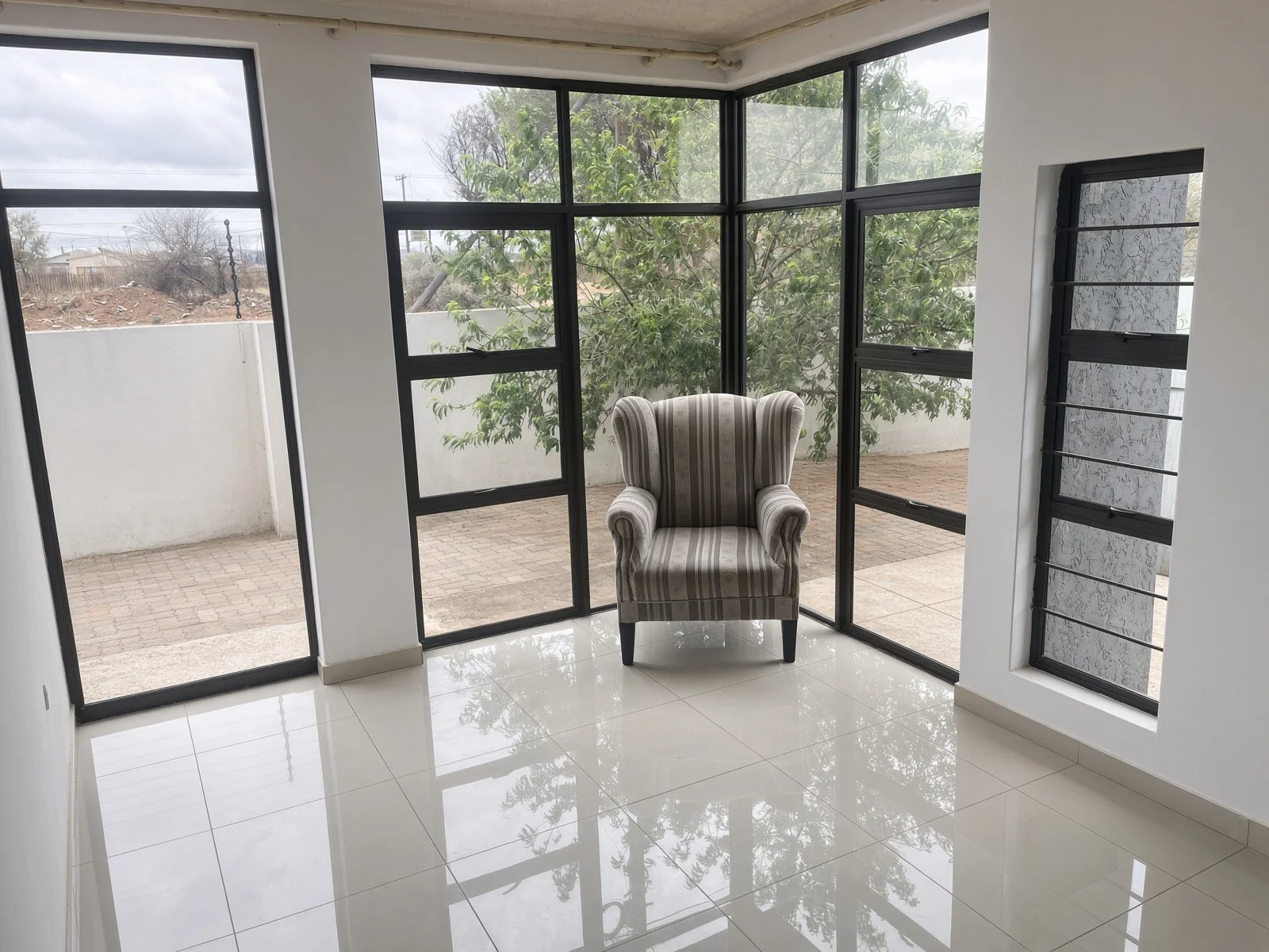 Corner sunroom with floor-to-ceiling windows, garden views and feature armchair, Gaborone property for sale