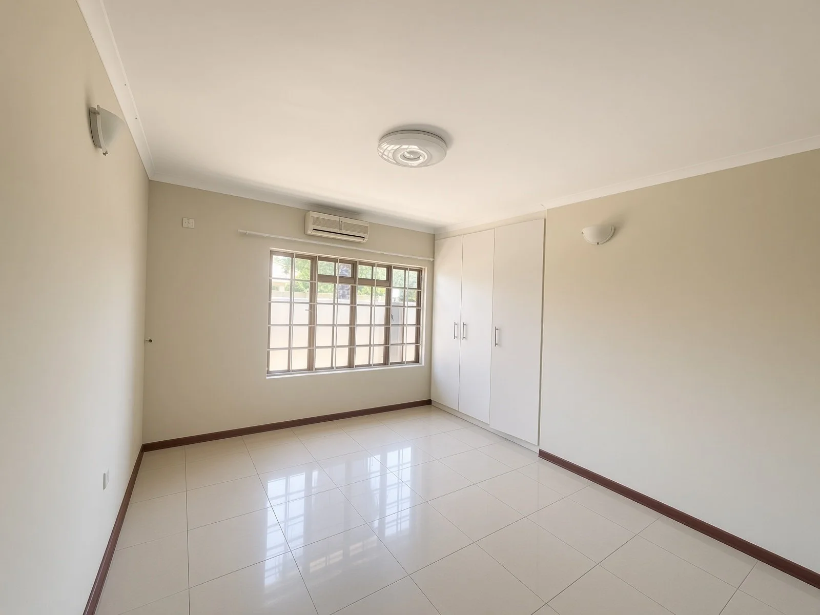 Bedroom with built-in white cupboards, air conditioning and barred window in a Phakalane house for rent