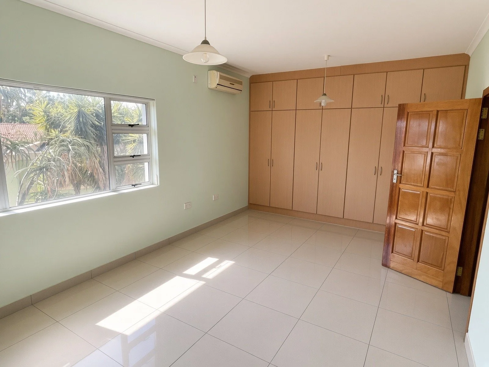 Bedroom with floor-to-ceiling fitted wardrobes, wooden door and air conditioning in the 4-bedroom house for rent, Phakalane gated estate. Nestgeeks.