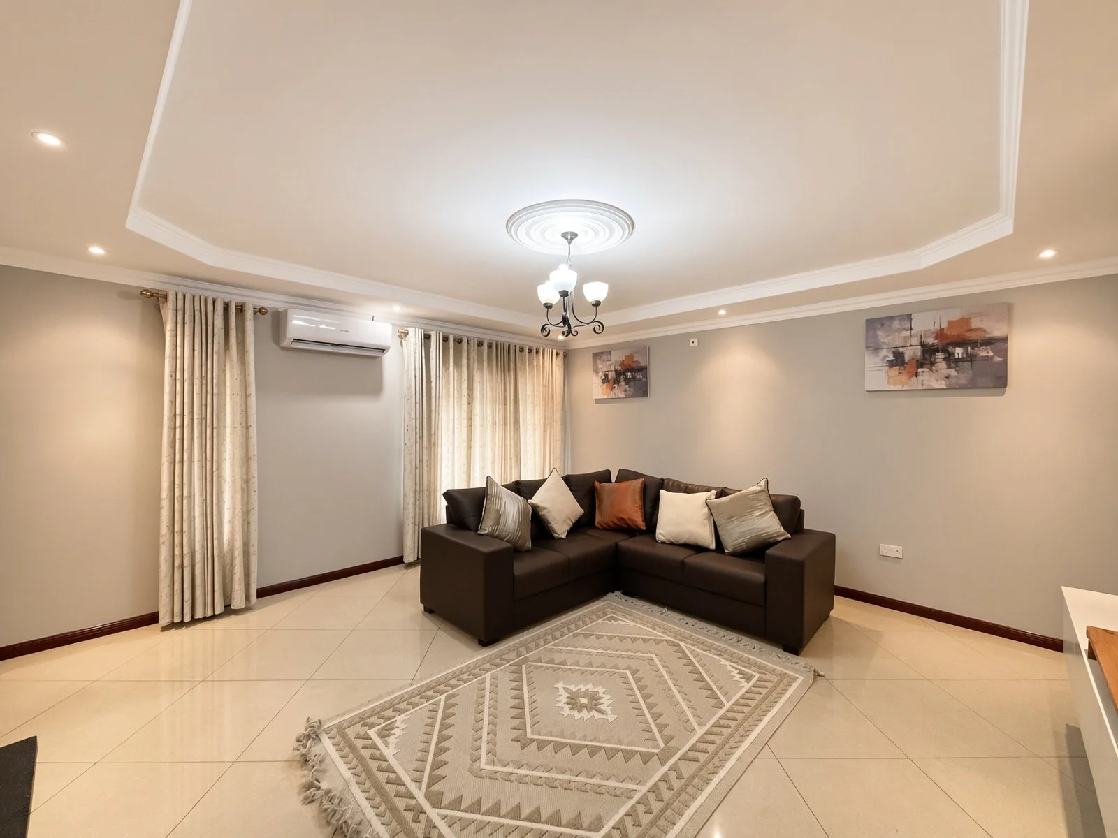 Comfortable air-conditioned lounge with brown sofa, curtains and ceiling lights in the 5-bedroom furnished rental, Phakalane. Nestgeeks.