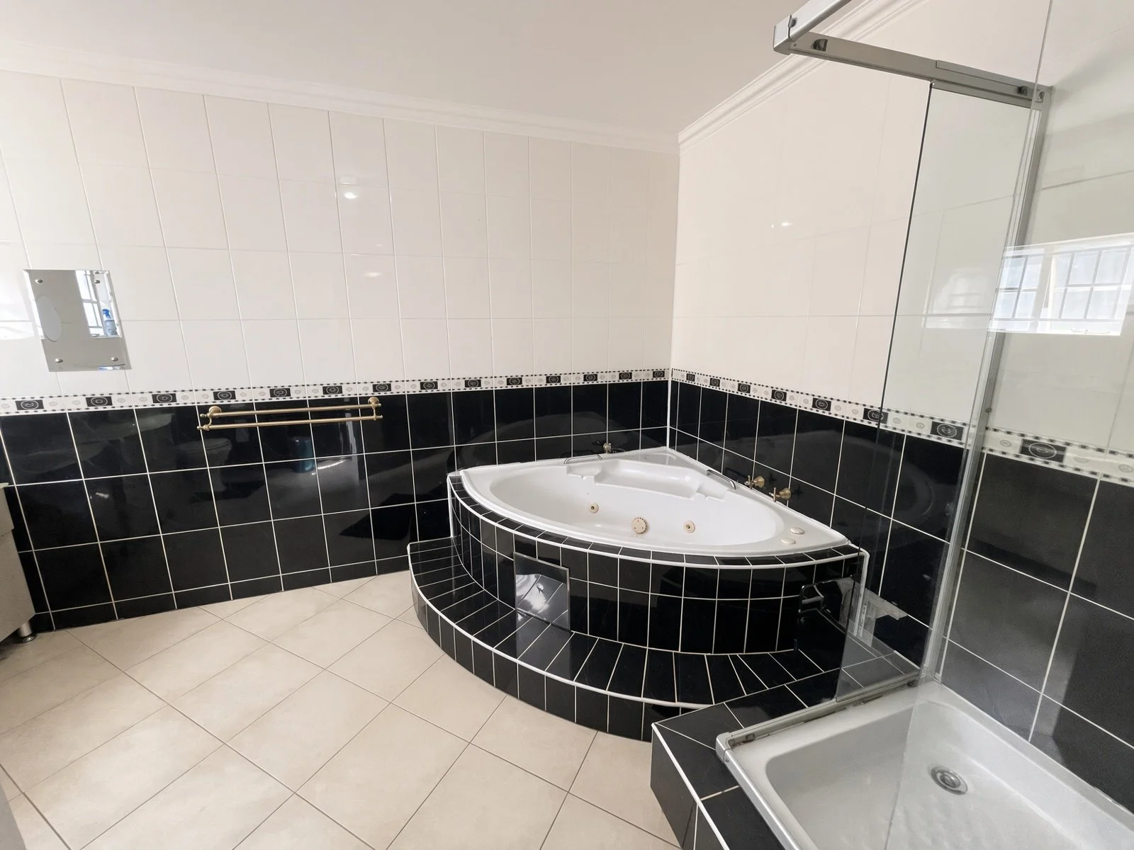 Master ensuite bathroom with corner jacuzzi bath, glass shower and black-and-white tiling in the 5-bedroom furnished rental, Phakalane. Nestgeeks.