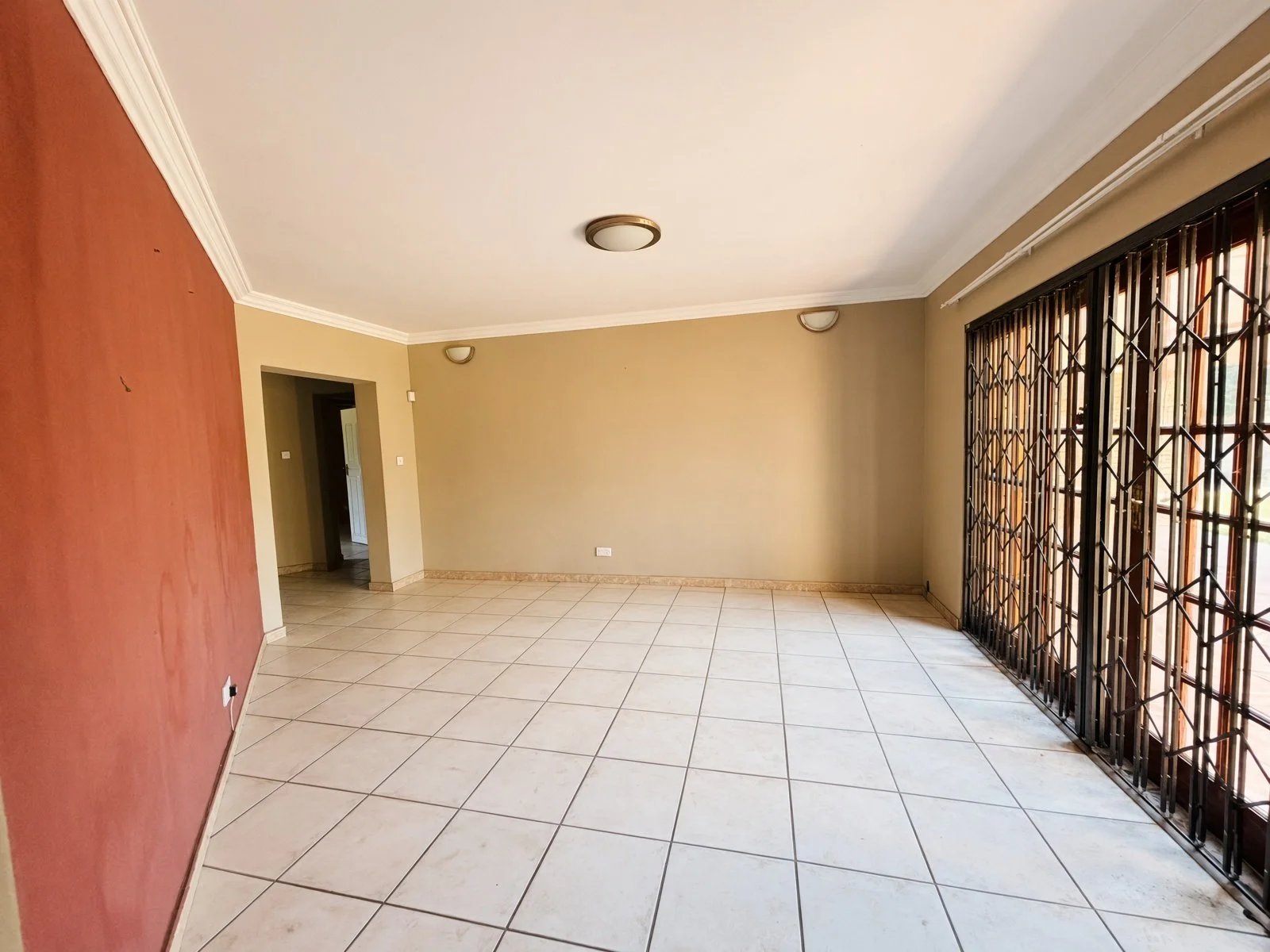 Tiled room with red accent wall and security gate in a 5-bedroom Phakalane home for sale