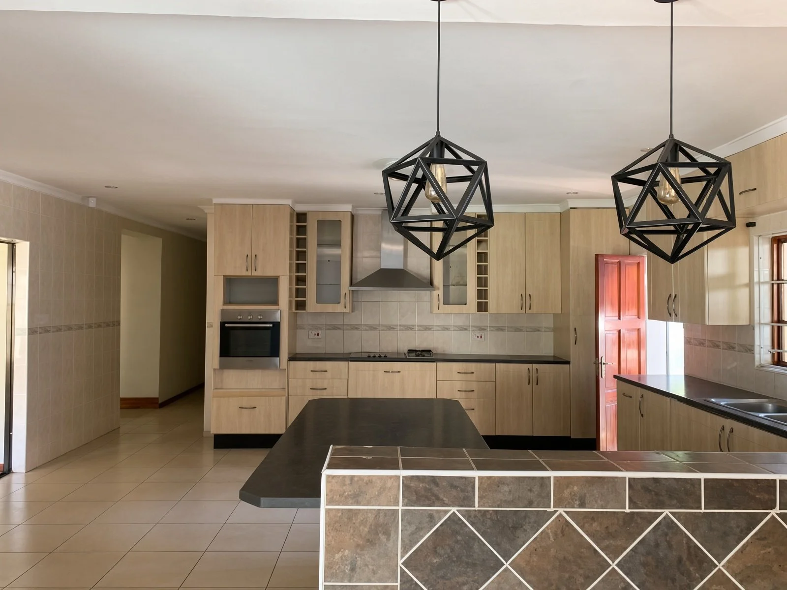 Fitted light-wood kitchen with black island, extractor and geometric pendant lights in a 4-bedroom house for rent in Phakalane