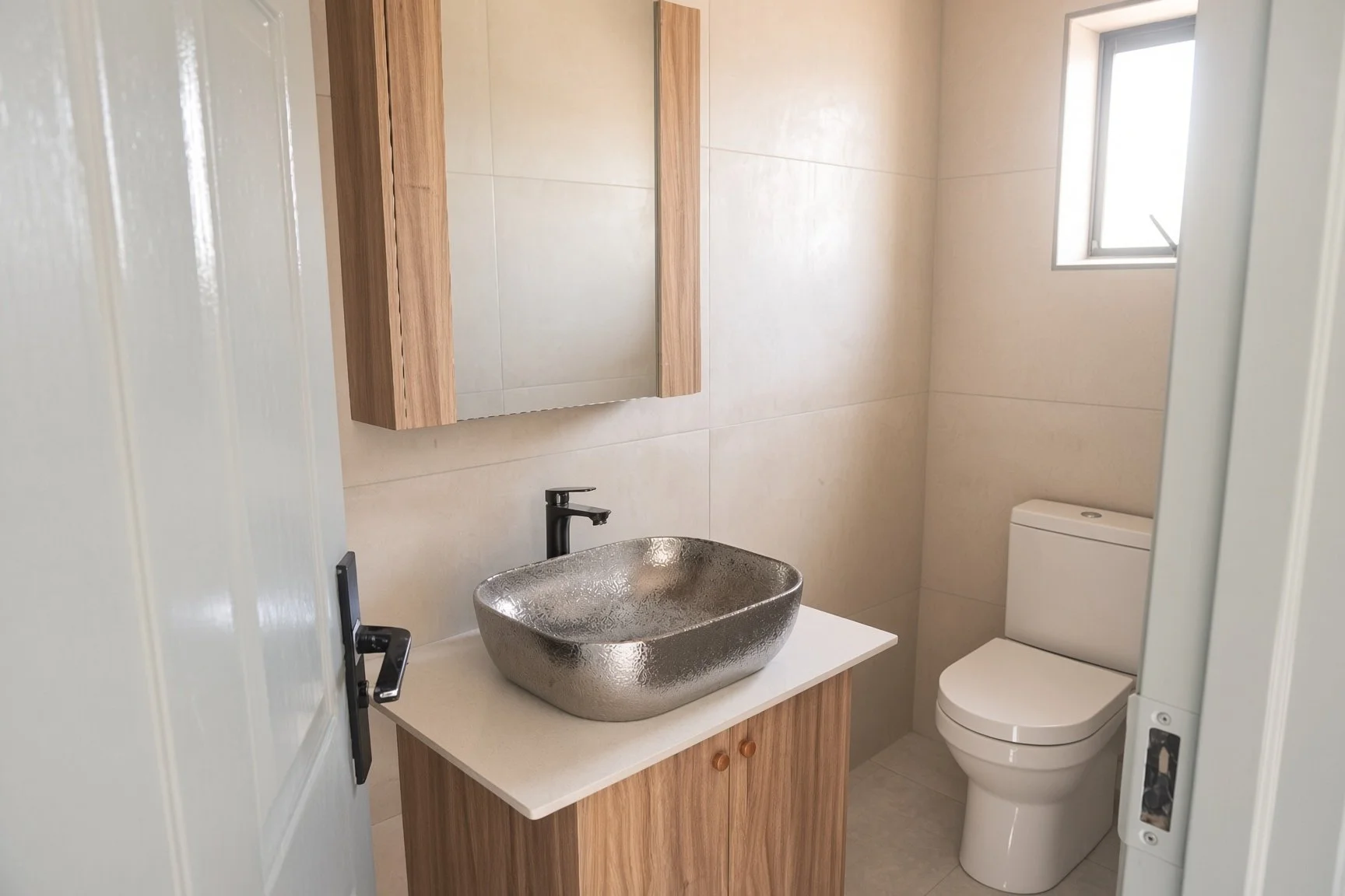 Guest toilet with hammered silver vessel sink, wooden vanity and beige tiled walls inside the 3-bedroom rental home in a secure gated estate, Gaborone North. Available through Nestgeeks.