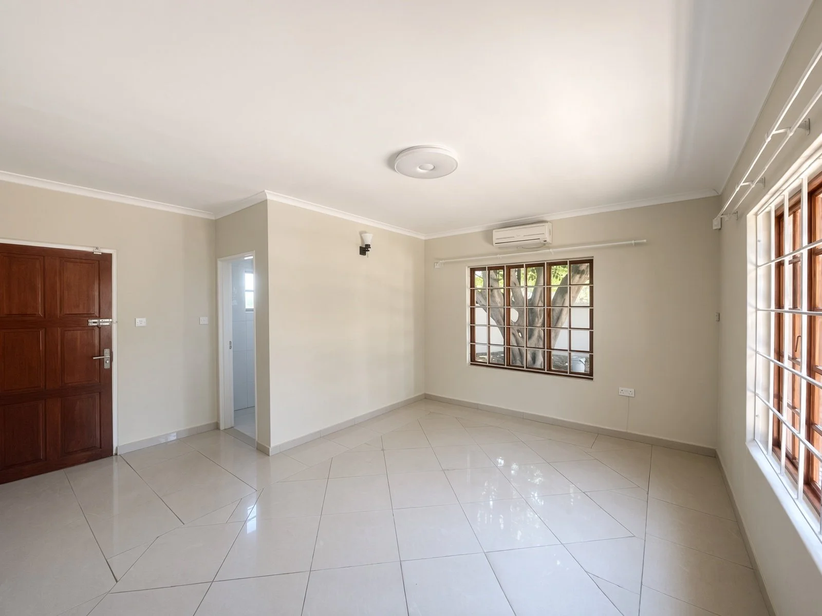 Spacious bedroom with air conditioning and wooden door in a 4-bedroom house for rent in Phakalane