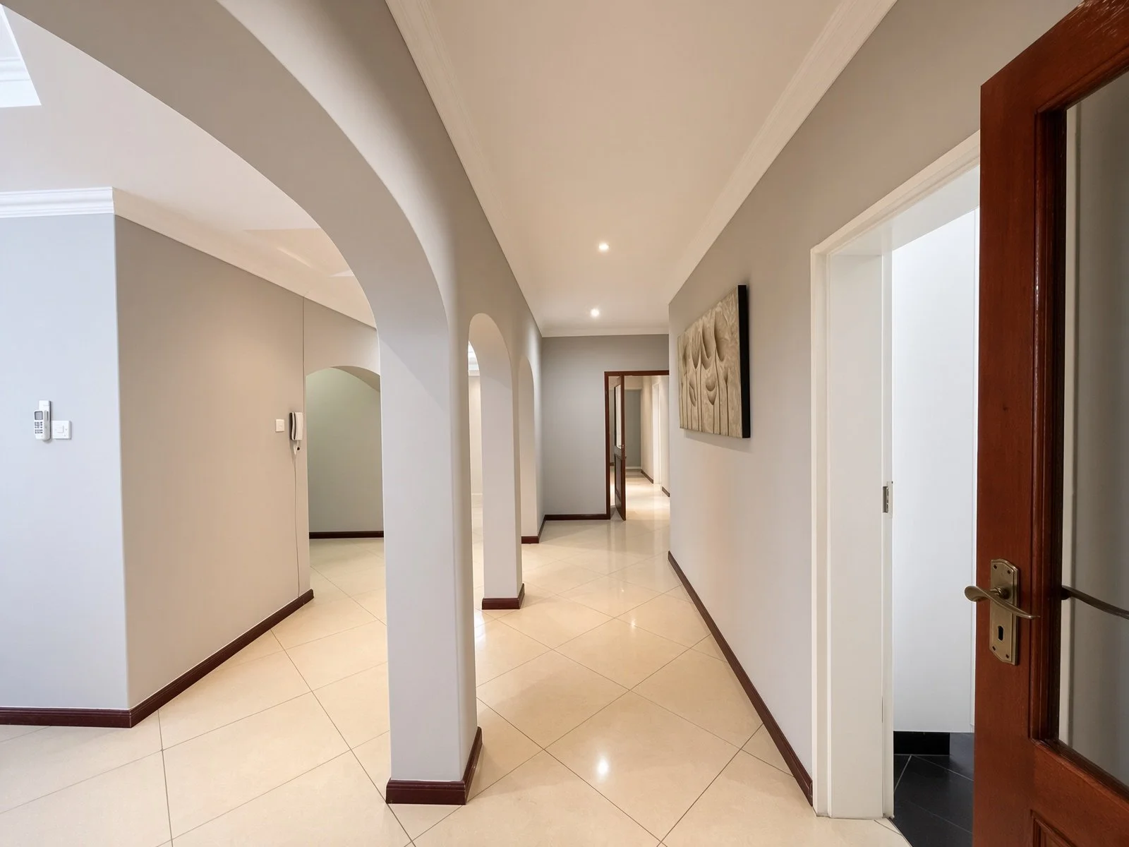 Spacious arched hallway with tiled floors and wooden doors leading through the fully furnished 5-bedroom rental home in Phakalane. Secure estate living with Nestgeeks.