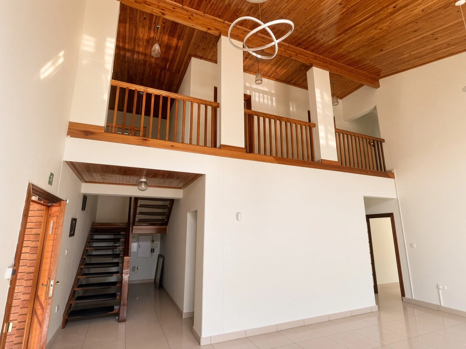 Double-volume living space with mezzanine balcony, wooden railing and staircase in the 4-bedroom gated-estate home, Phakalane. Nestgeeks.