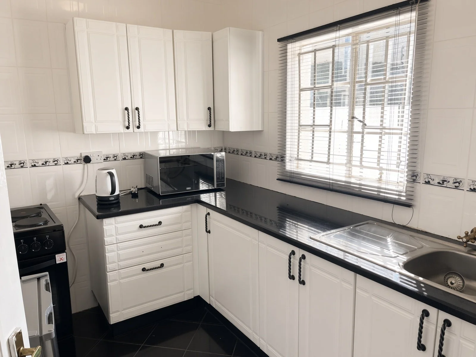 Private kitchenette with white cabinets, black granite worktop, stove and microwave — part of the fifth bedroom guest suite in this 5-bedroom Phakalane rental. Nestgeeks.