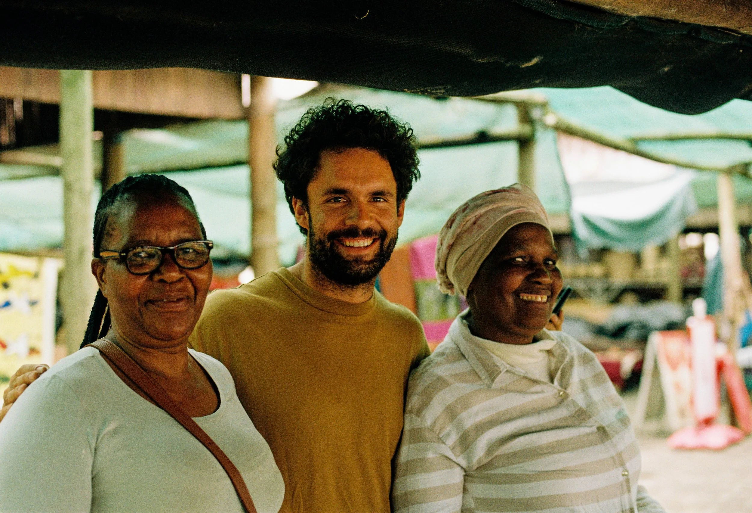 Three people smiling and standing together outdoors at a market.