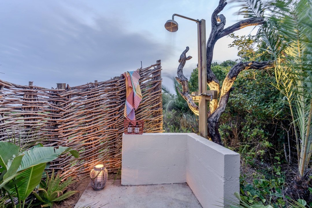 Outdoor shower with wooden privacy fence, colorful towel, lantern, and plants.