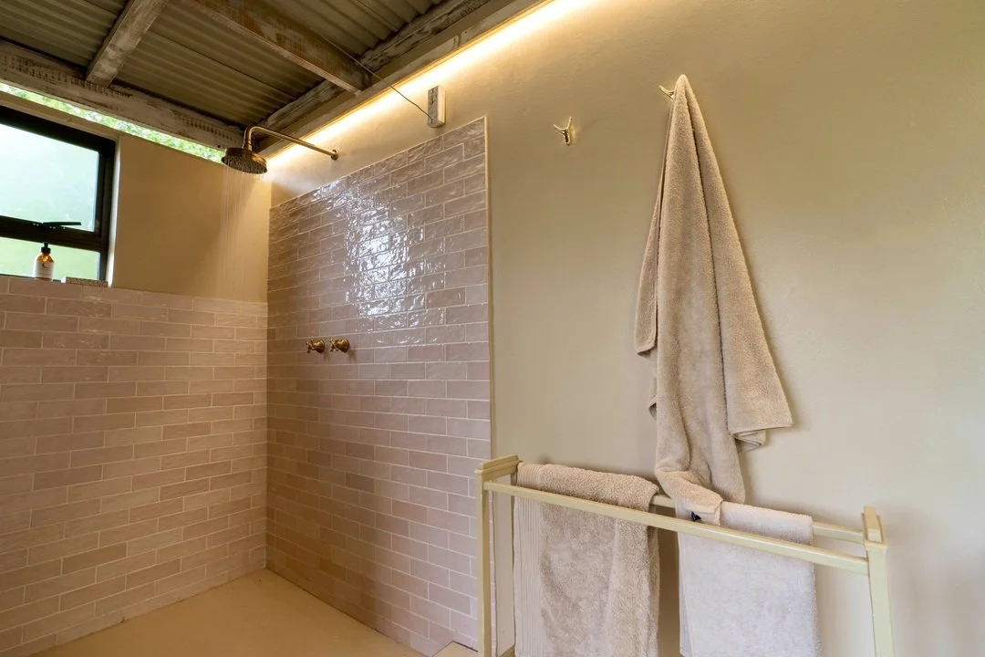 Modern bathroom with rain shower, beige tiled walls, beige towels on a rack, and a wall-mounted towel hook.