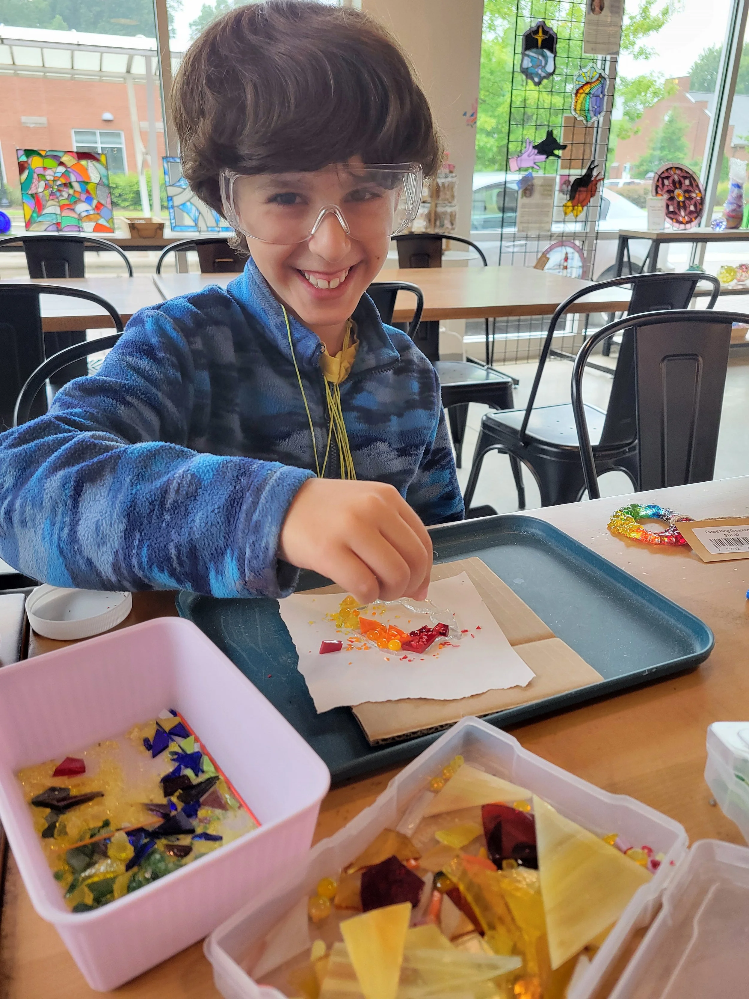 Pictured is a chlid class participant arranging glass pieces while seated in a sunny gallery room. 