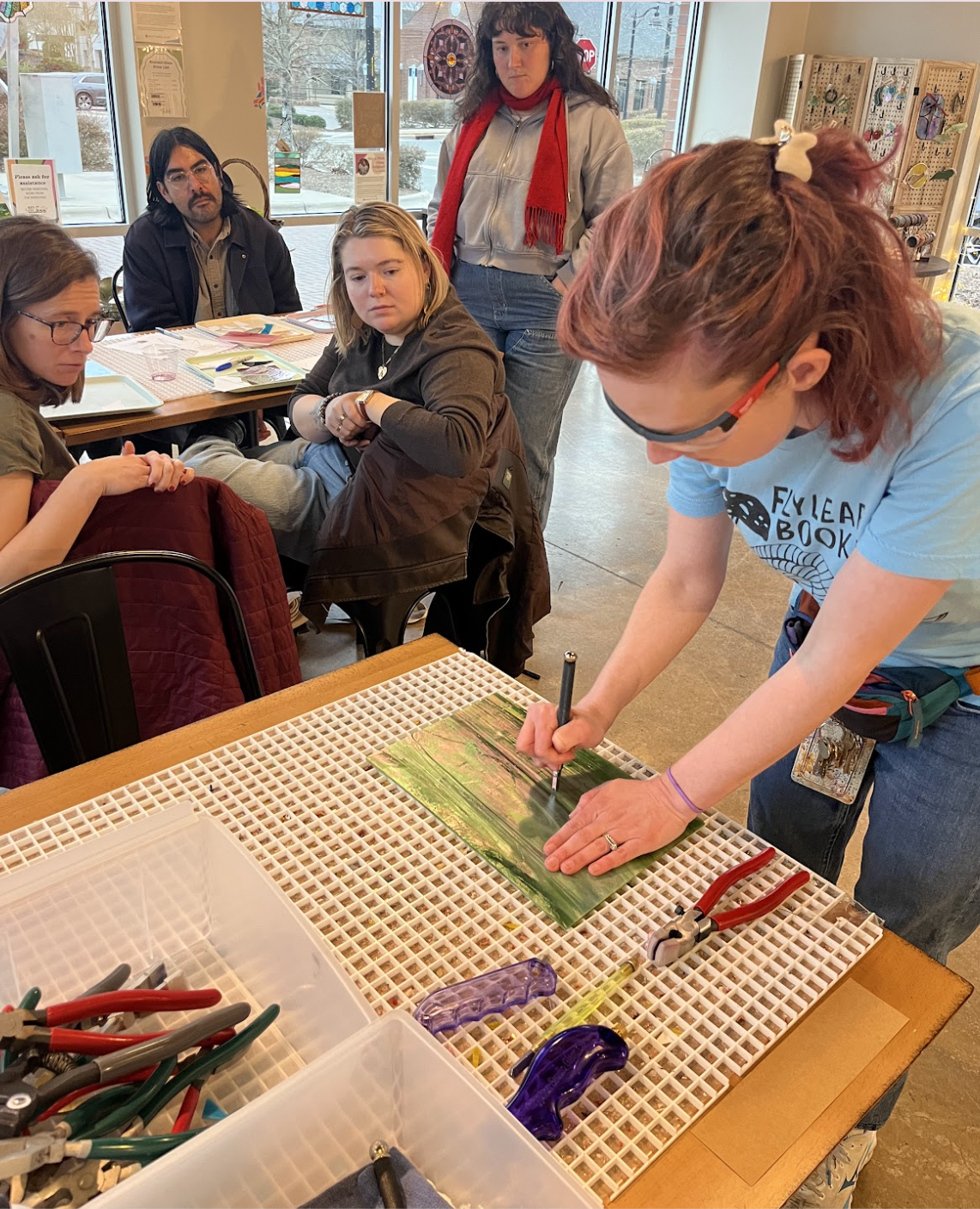 An instructor demonstrates how to cut a piece of glass as three students observe.
