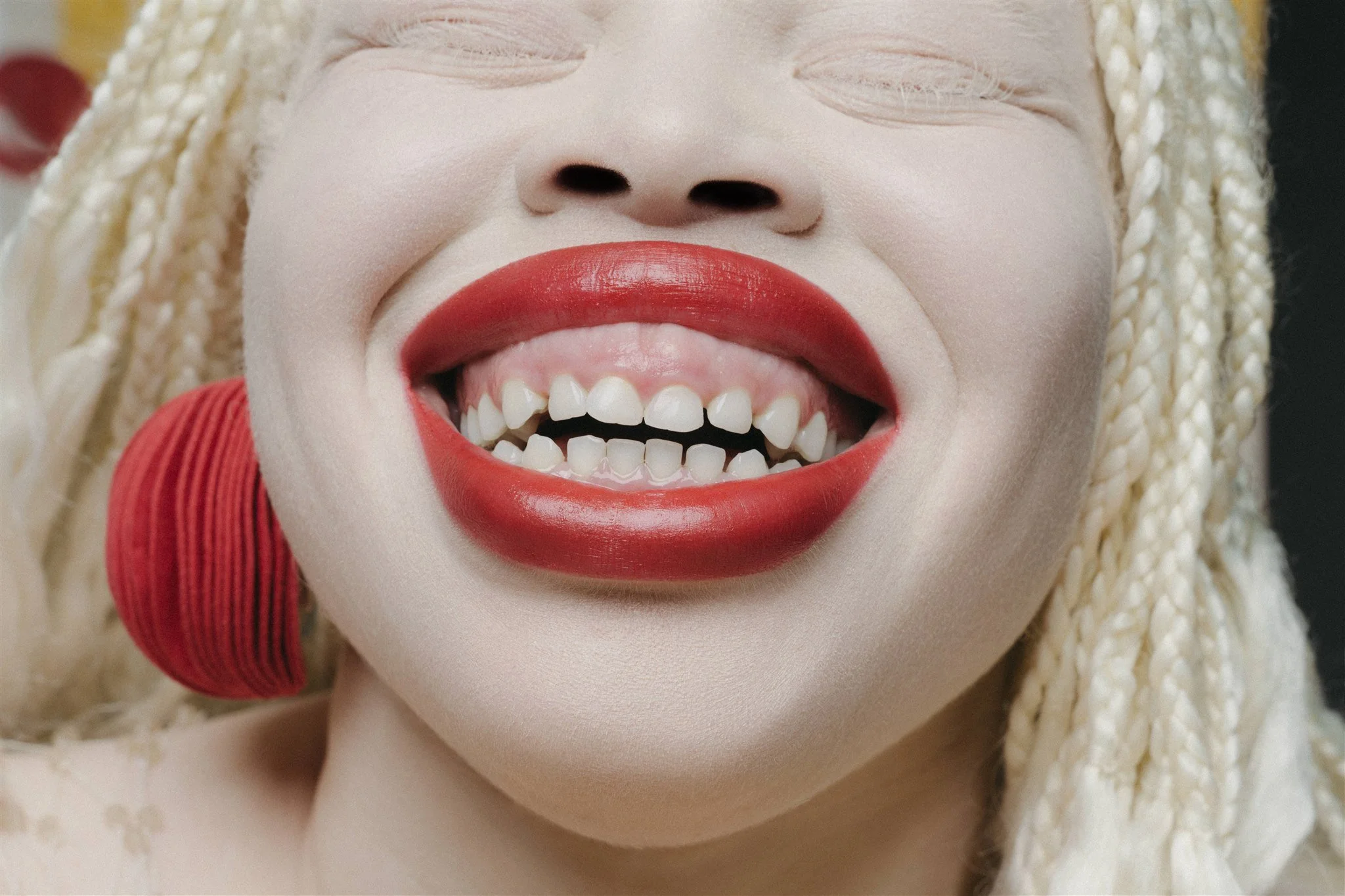 Gros plan d'un visage souriant avec rouge à lèvres rouge et grandes boucles d'oreilles rouges.