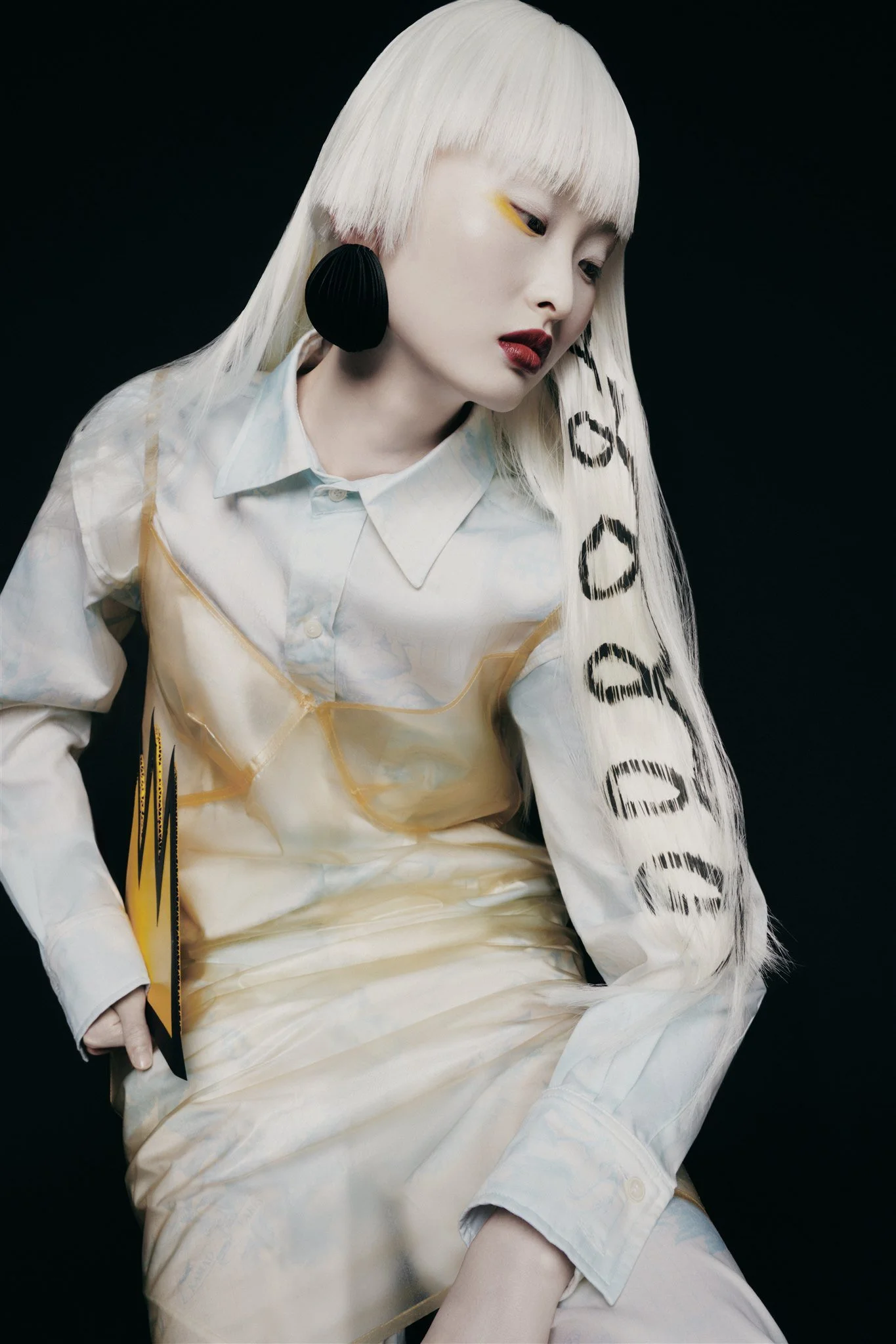 Personne avec cheveux blancs longs, vêtue d'une chemise blanche et d'une robe transparente, sur fond noir.