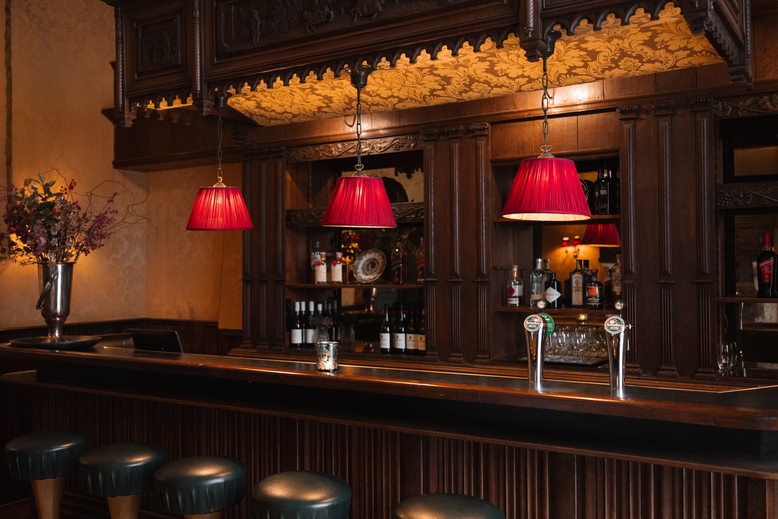 Empty bar with dark wood cabinets, red hanging pendant lamps, and beer taps in a cozy, dimly lit setting.