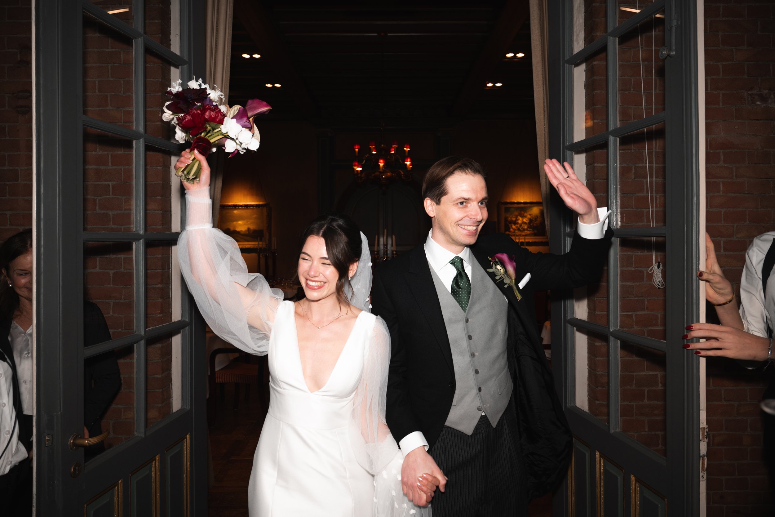 Happy bride and groom holding hands and smiling as they leave a wedding venue.