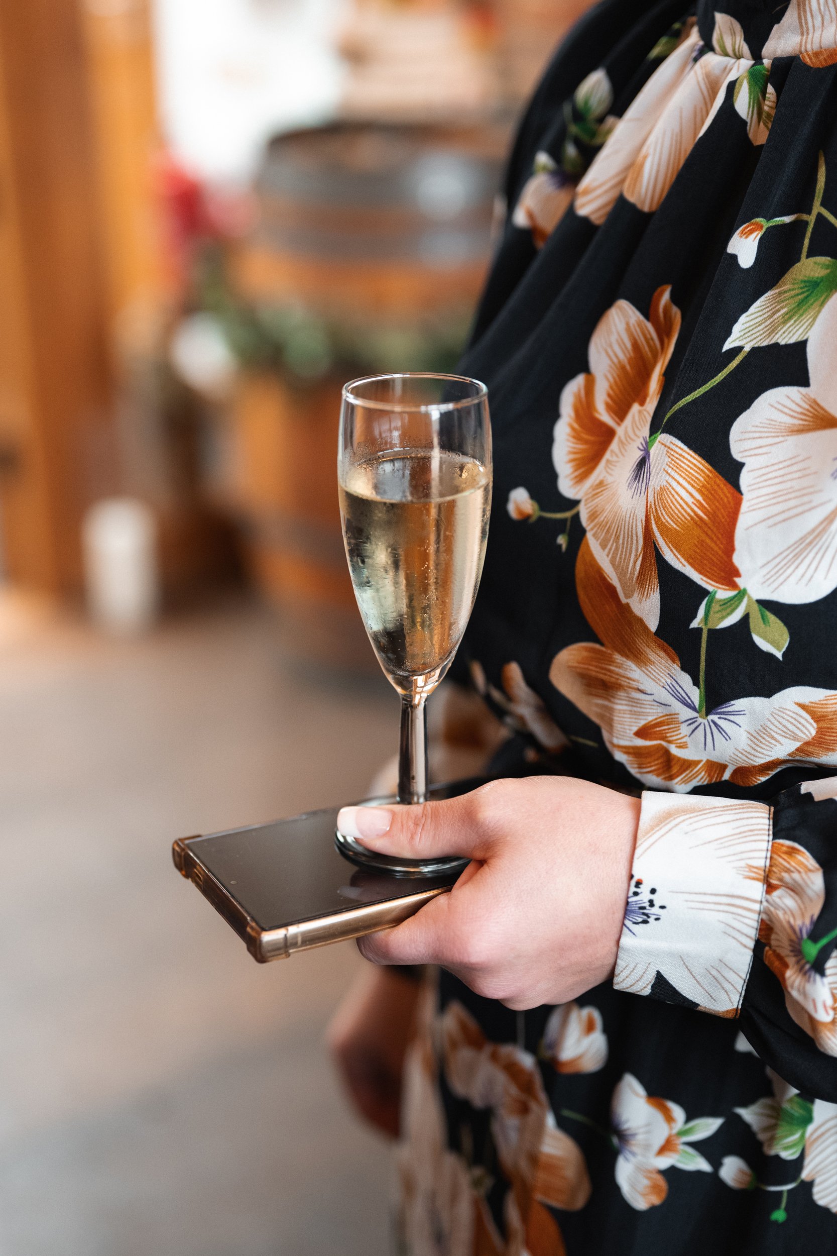 Person holding a smartphone with a glass of champagne resting on it, wearing a floral patterned shirt.