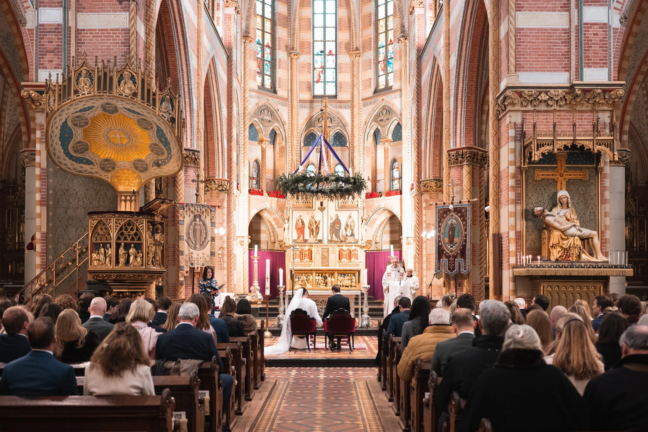 A wedding ceremony taking place inside a church with ornate architecture, stained glass windows, a congregation seated in pews, and a bride and groom at the altar.