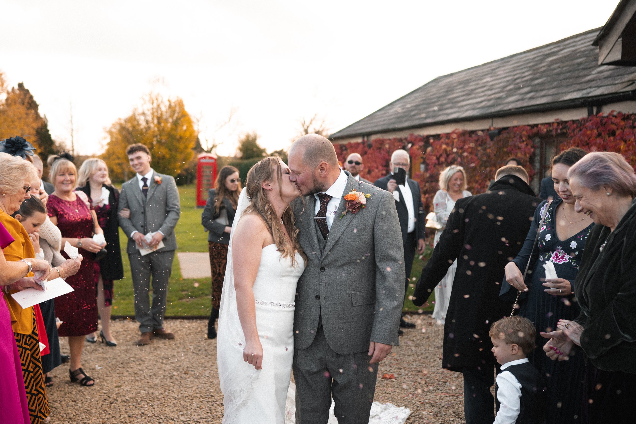 A newlywed couple kisses during their outdoor wedding ceremony with guests celebrating around them.