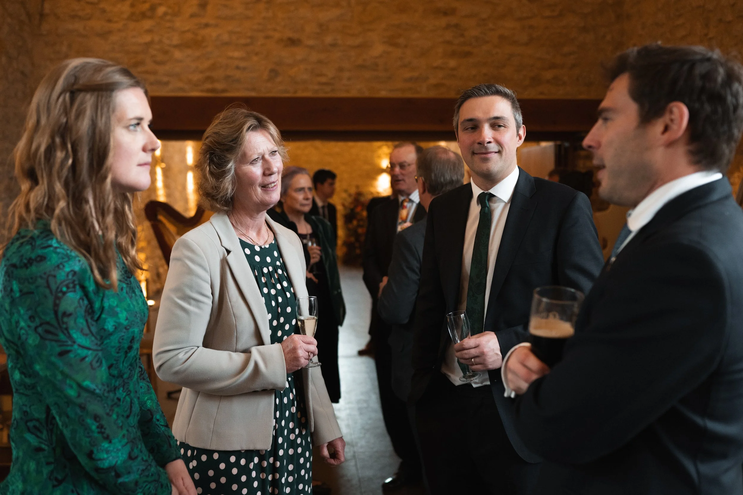 Group of people dressed in formal attire socializing at an indoor event, holding glasses of wine and beer.