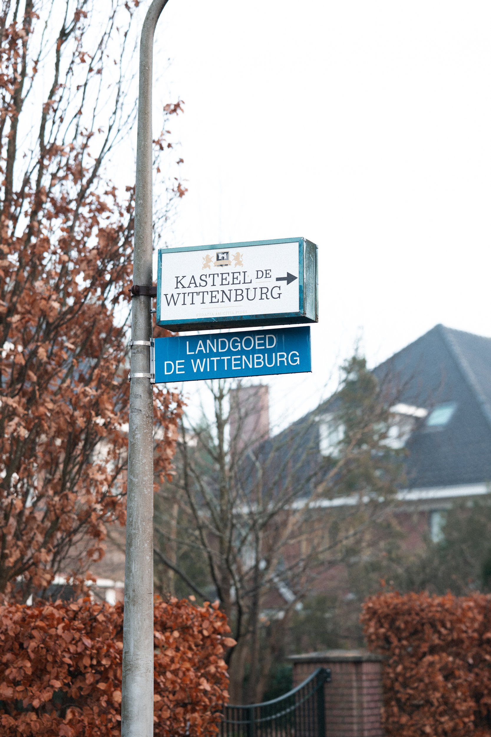 Street signs indicating directions to Kasteel de Wittenburg and Landoed de Wittenburg in a neighborhood with autumn-colored trees and houses in the background.