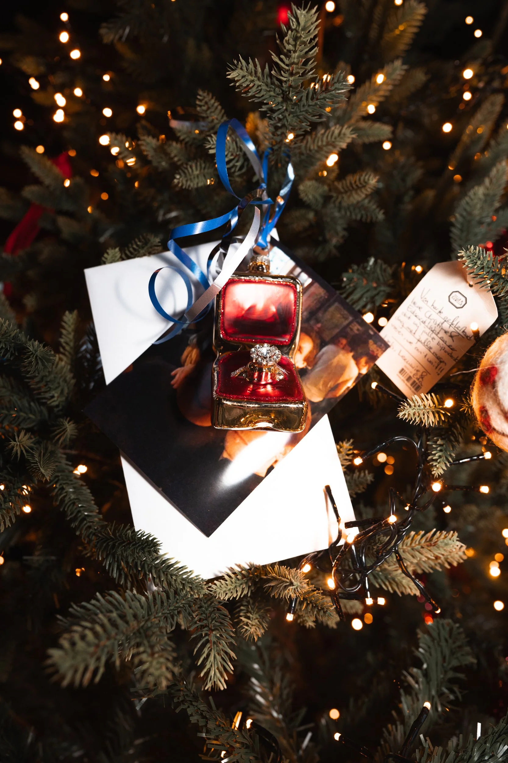 Christmas tree ornament featuring a ring in a red velvet box, hanging from branches decorated with lights and Christmas cards.