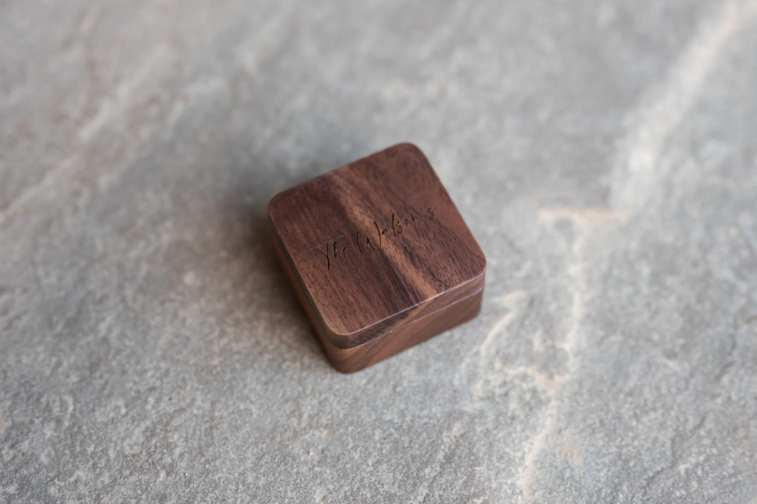 Small wooden box with engraved text 'The Witness' on top, placed on a gray stone surface.