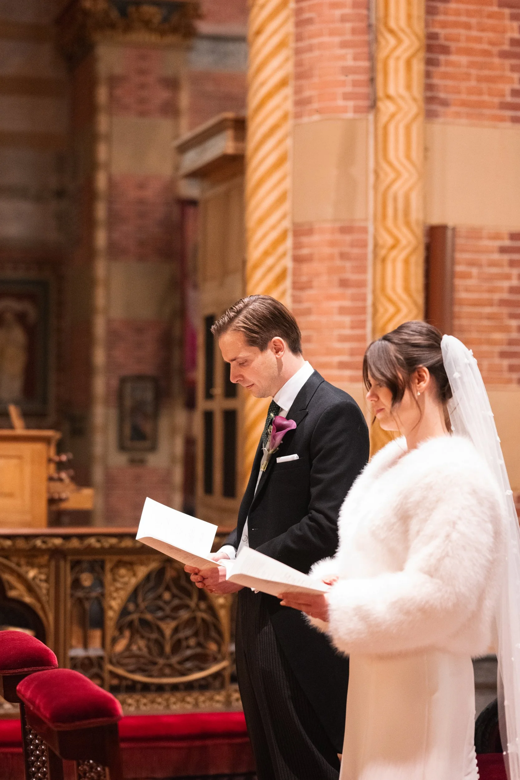 A bride and groom stand side by side in a church, reading from papers during their wedding ceremony.