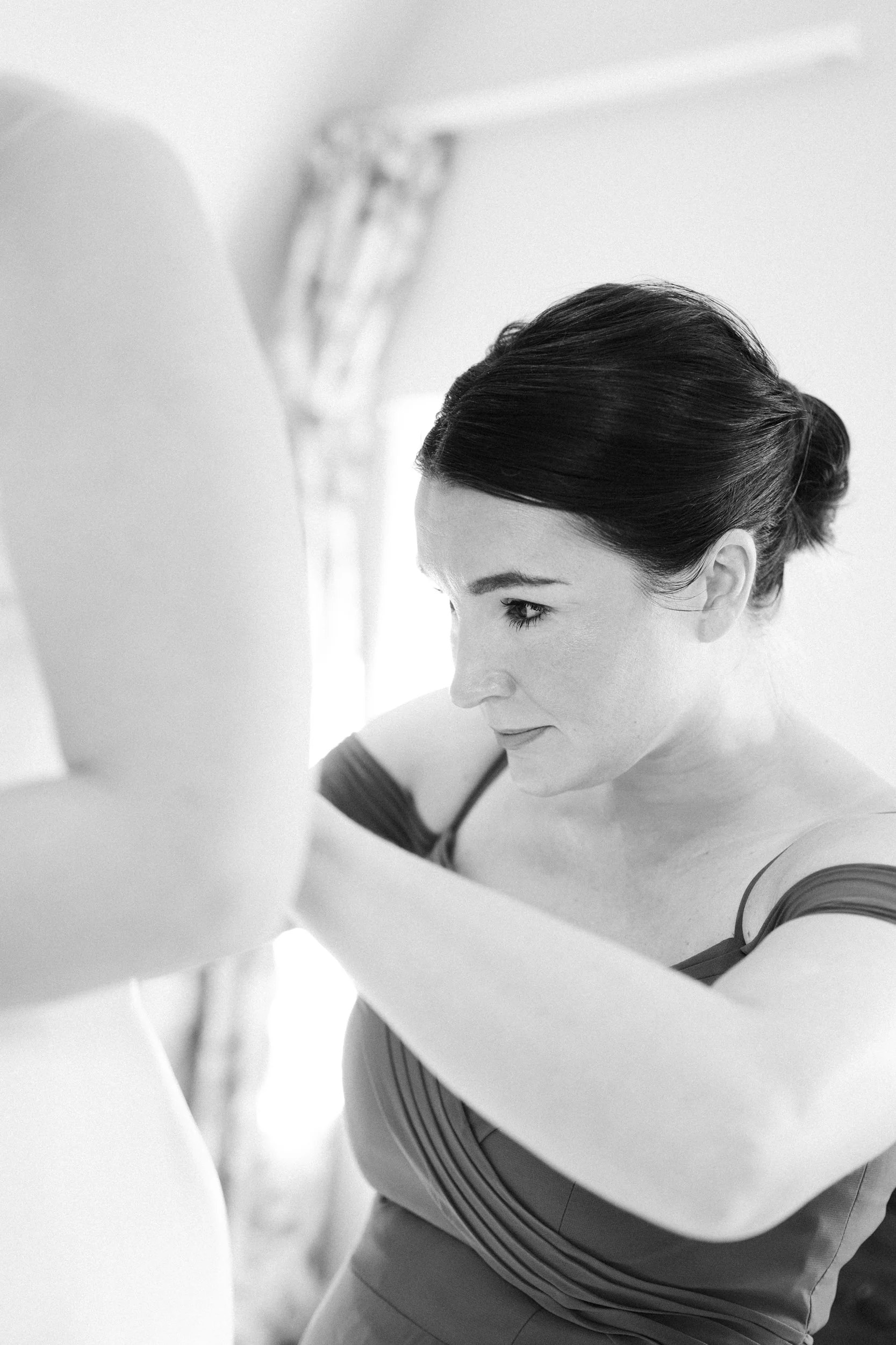 A woman with dark hair styled in an elegant updo, wearing a sleeveless dress with horizontal stripes, is adjusting a white wedding dress.