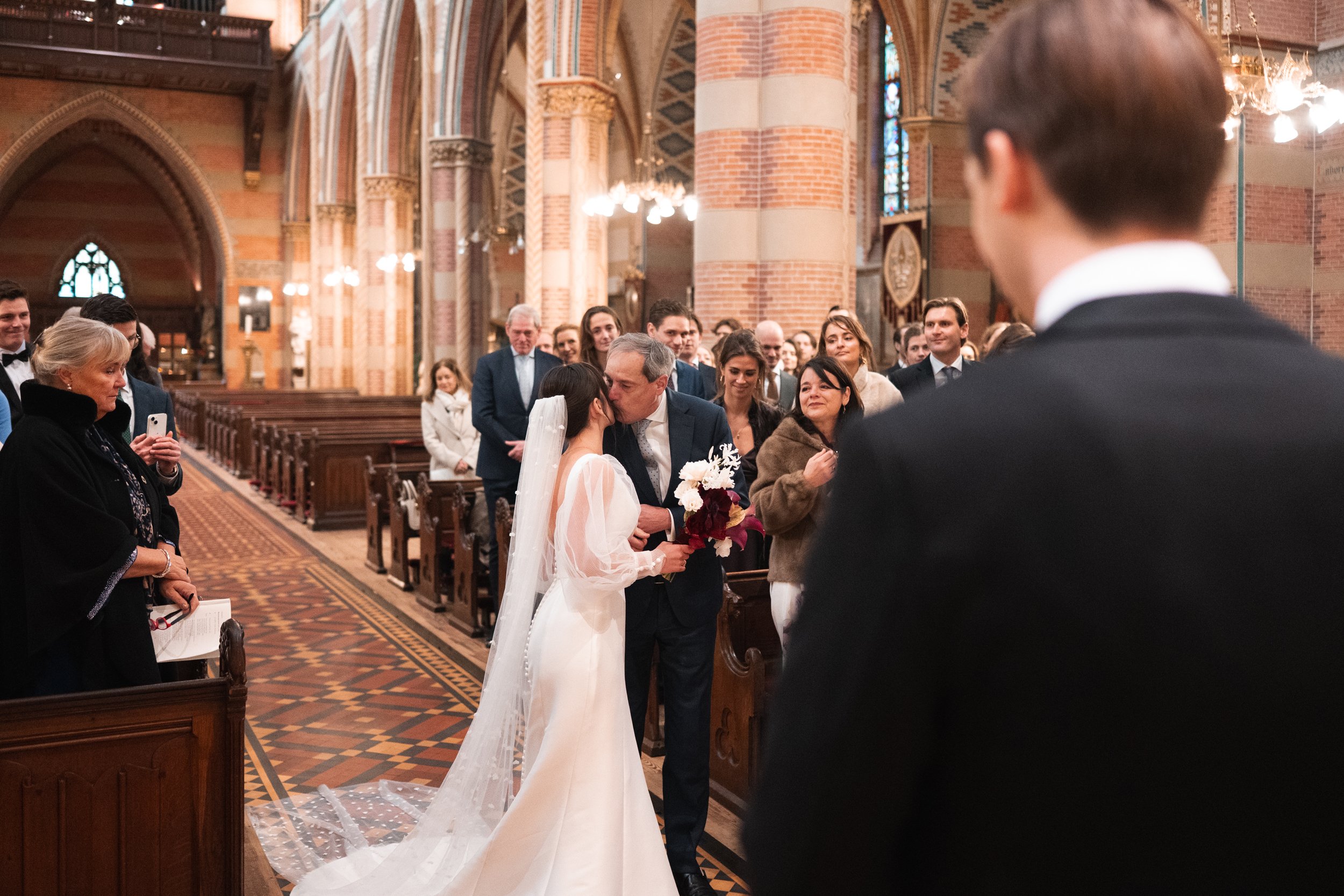 Bride kissing her father before wedding ceremony in a church filled with guests.
