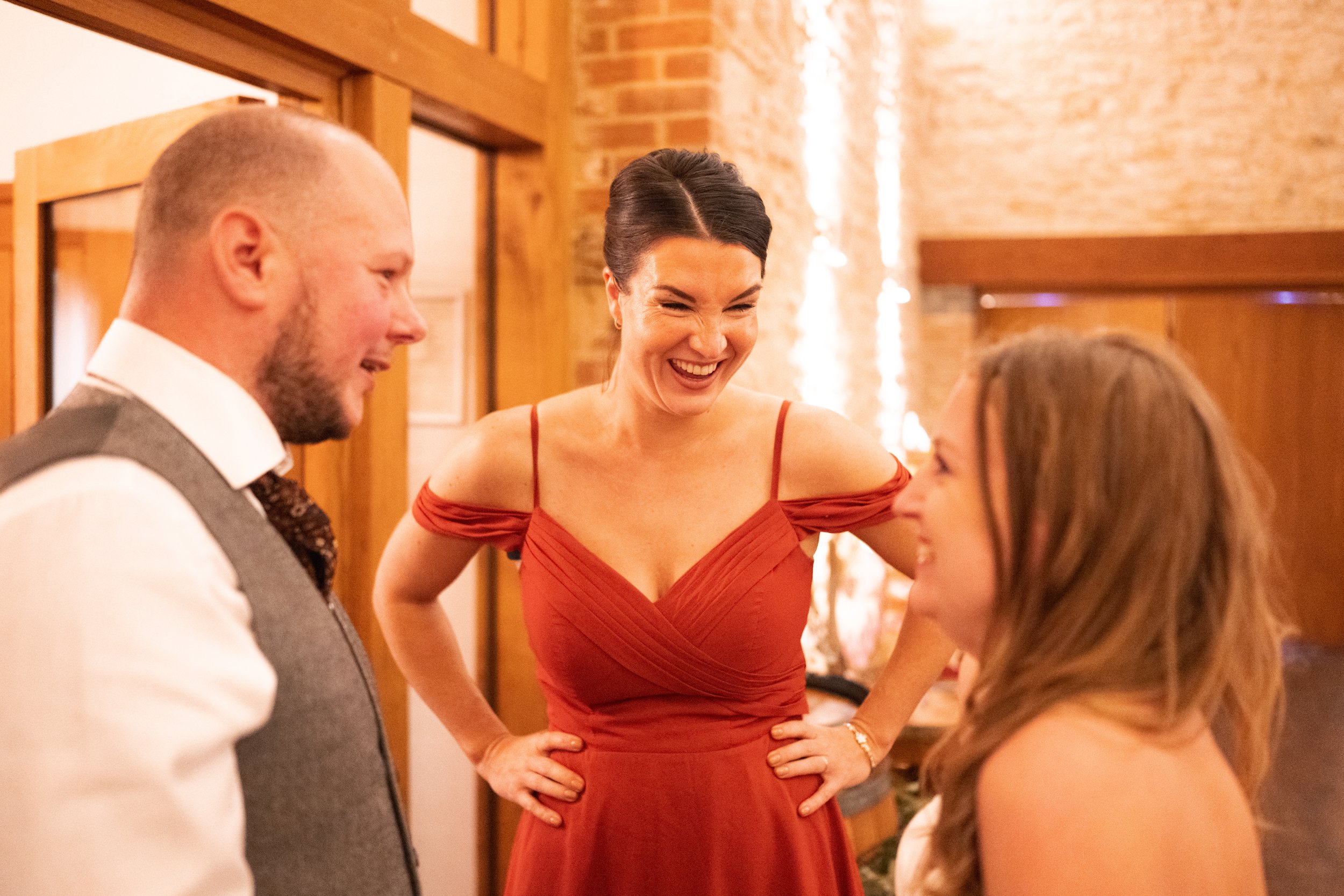 Three people laughing and talking at a social event in a warmly lit room with brick and wooden decor.