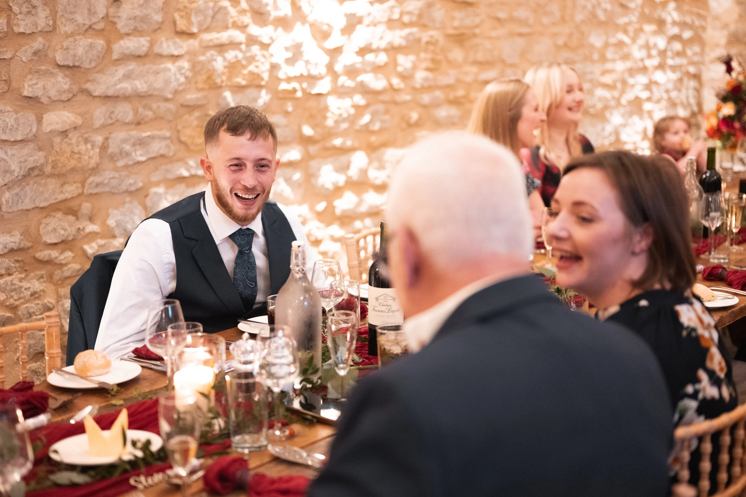 People sitting at a decorated dining table, smiling and enjoying a celebration in a rustic-style room with a brick wall background.